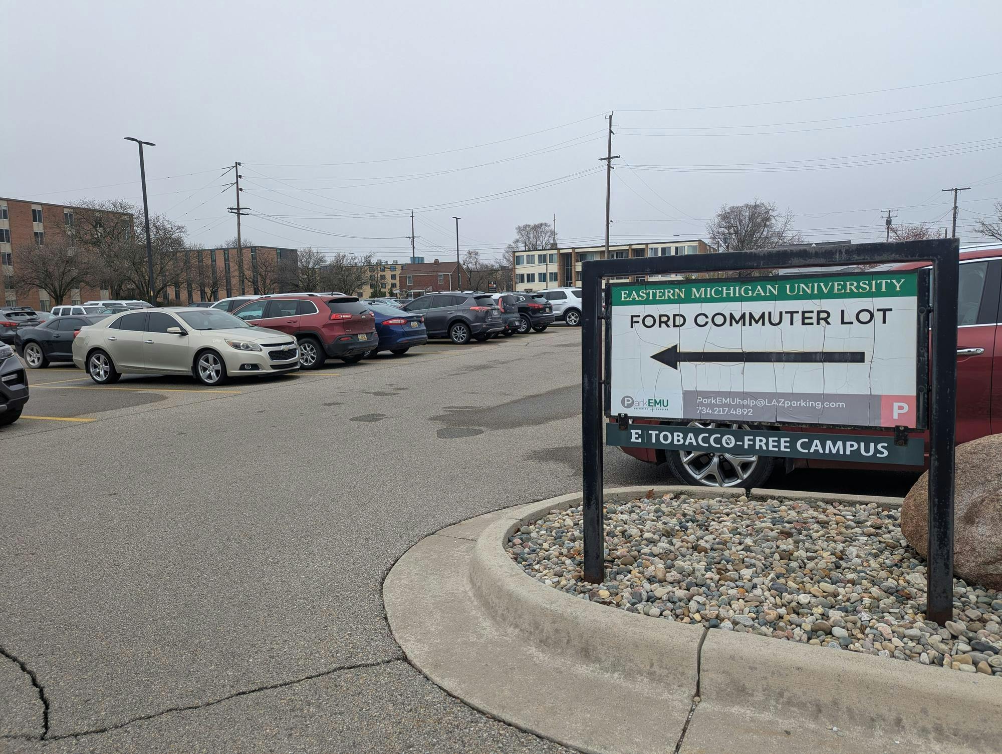 Parking lot full of parked cars. Parking sign reads, " Eastern Michigan University Ford Commuter Lot."