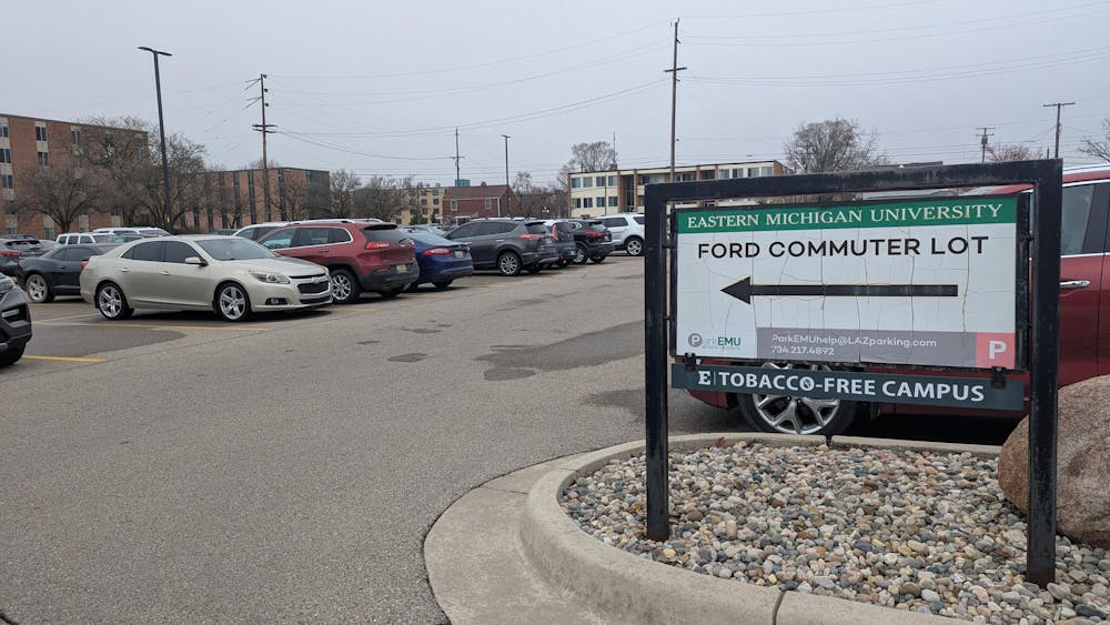 Parking lot full of parked cars. Parking sign reads, " Eastern Michigan University Ford Commuter Lot."