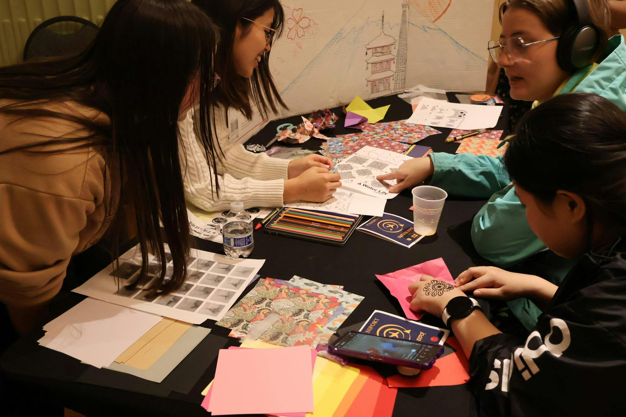 Four students crowd around a table creating origami out of paper. 