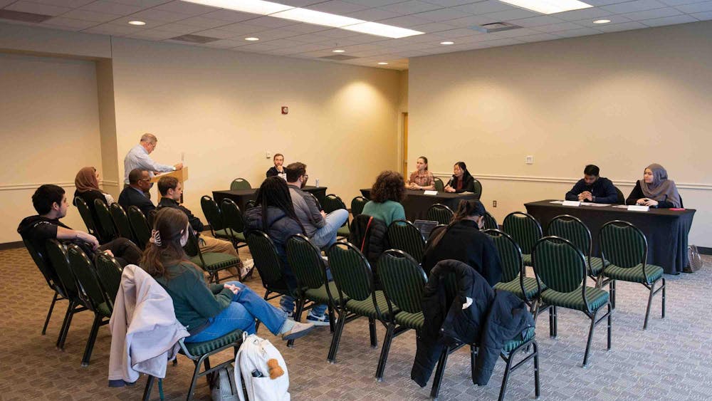 At two tables, candidates from each presidential ticket sit and answer questions. Attendees watch from rows of chairs.