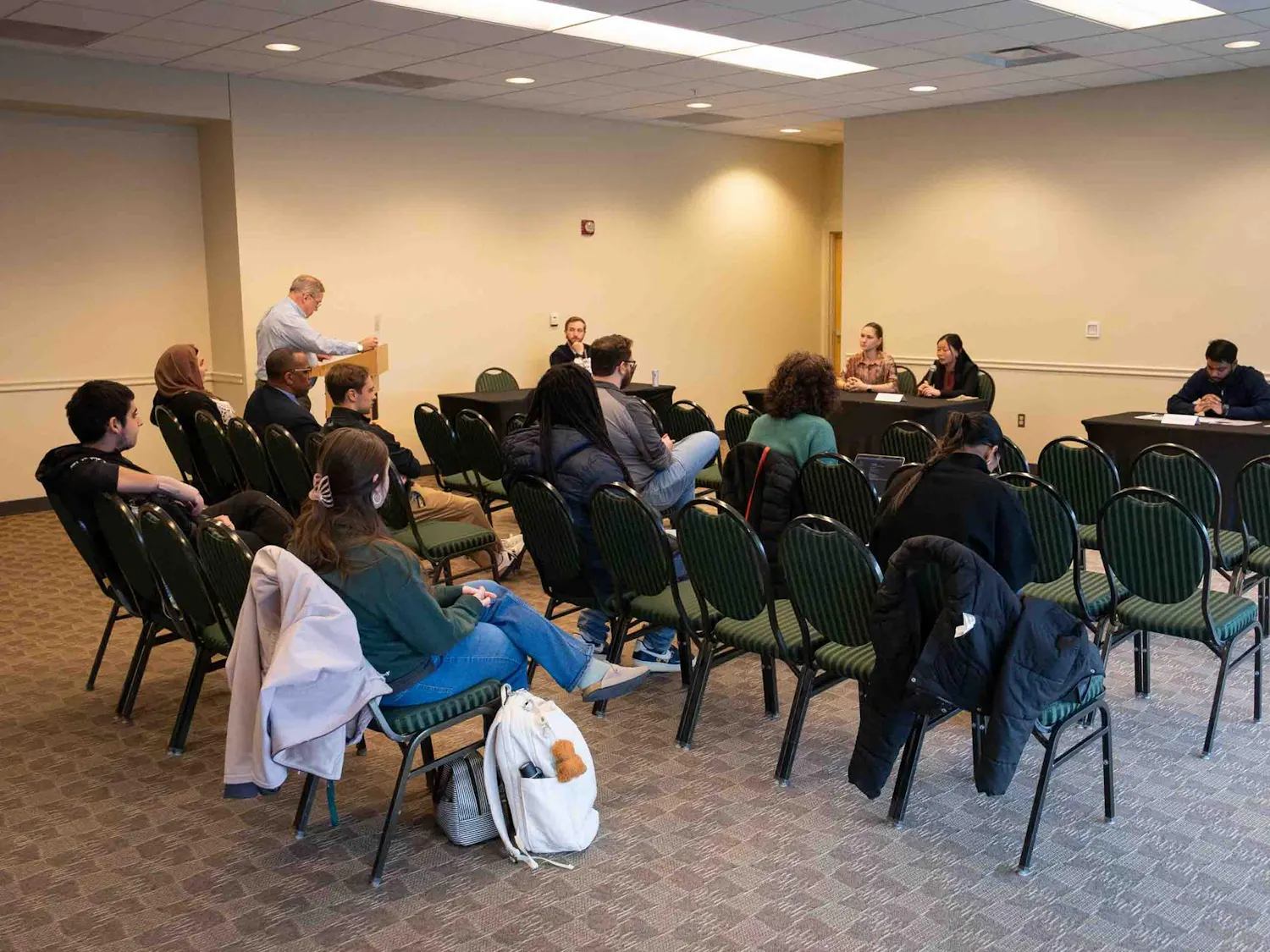 At two tables, candidates from each presidential ticket sit and answer questions. Attendees watch from rows of chairs.