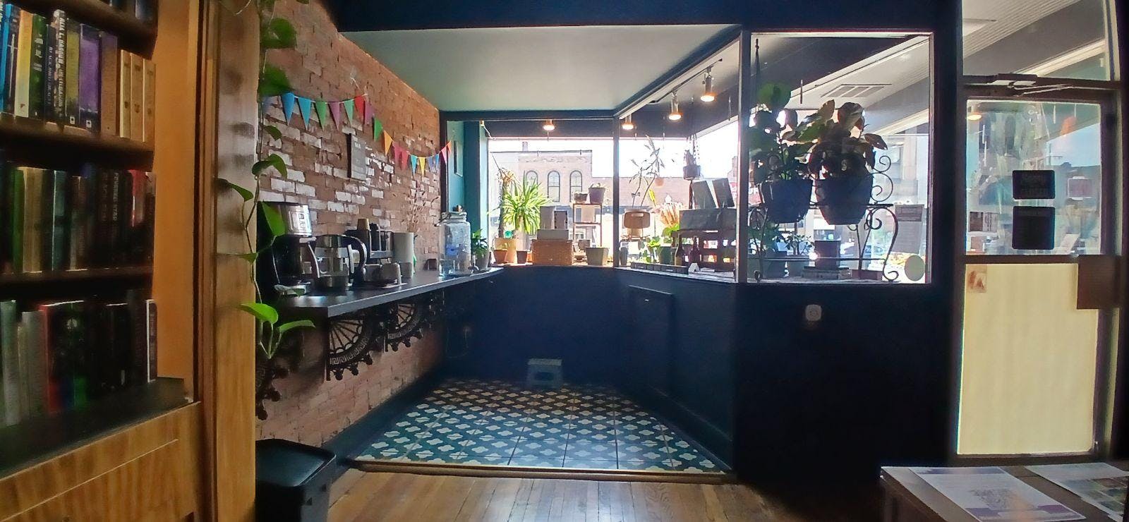Coffee and tea area on a counter in front of a window with plants in a book store. 