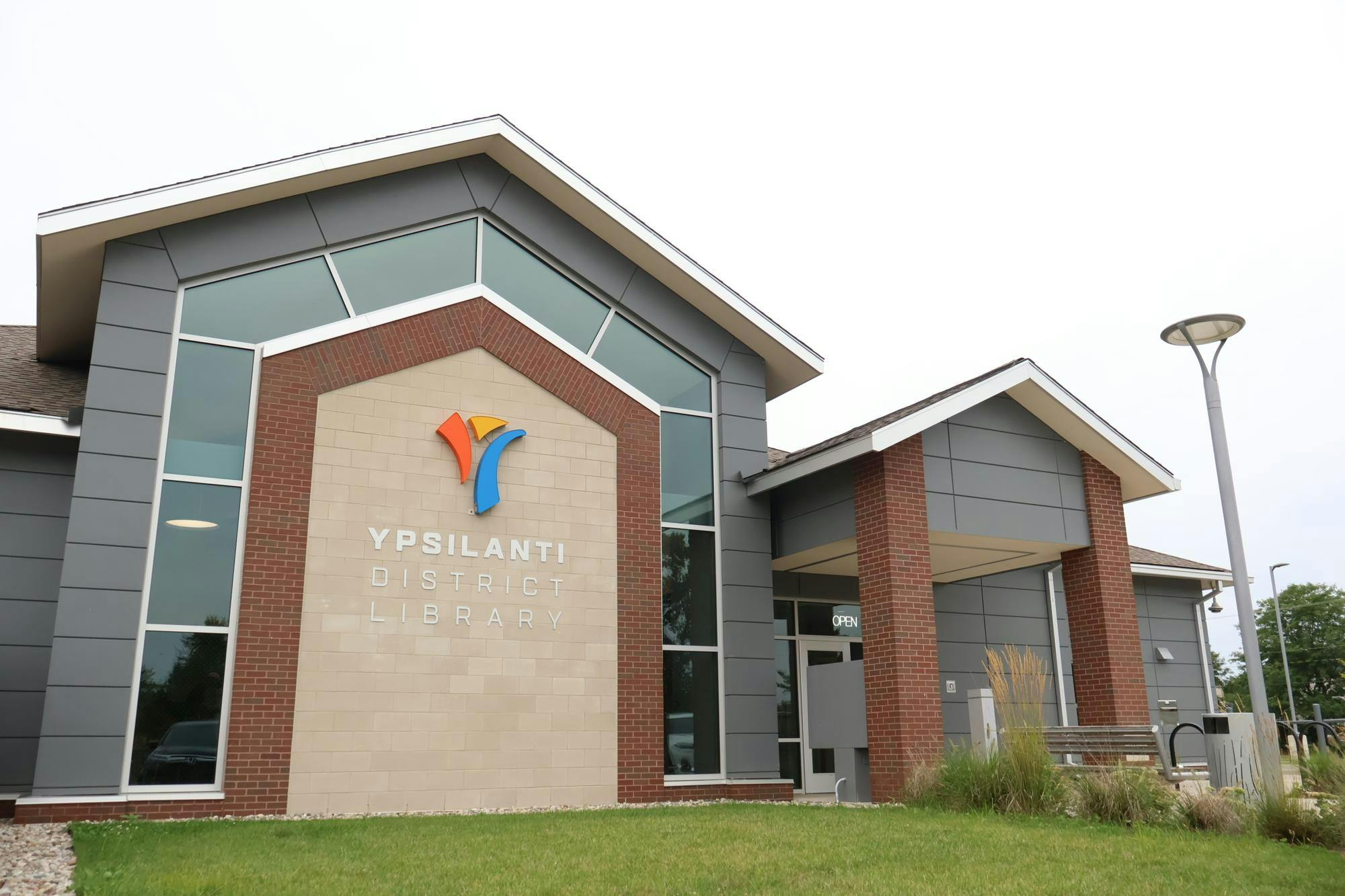 A gray building with glass and brick details with the Ypsilanti District Library logo on the side.