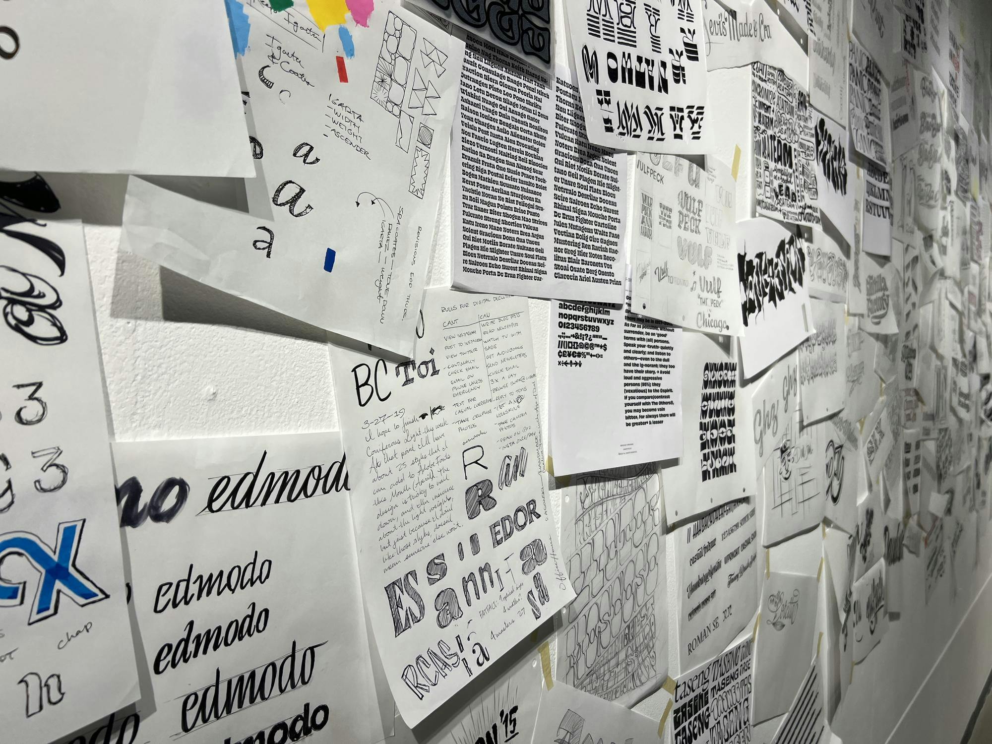 An angled shot of a wall that, within frame, is mostly covered in sketches and designs for typefaces made by James Edmondson.