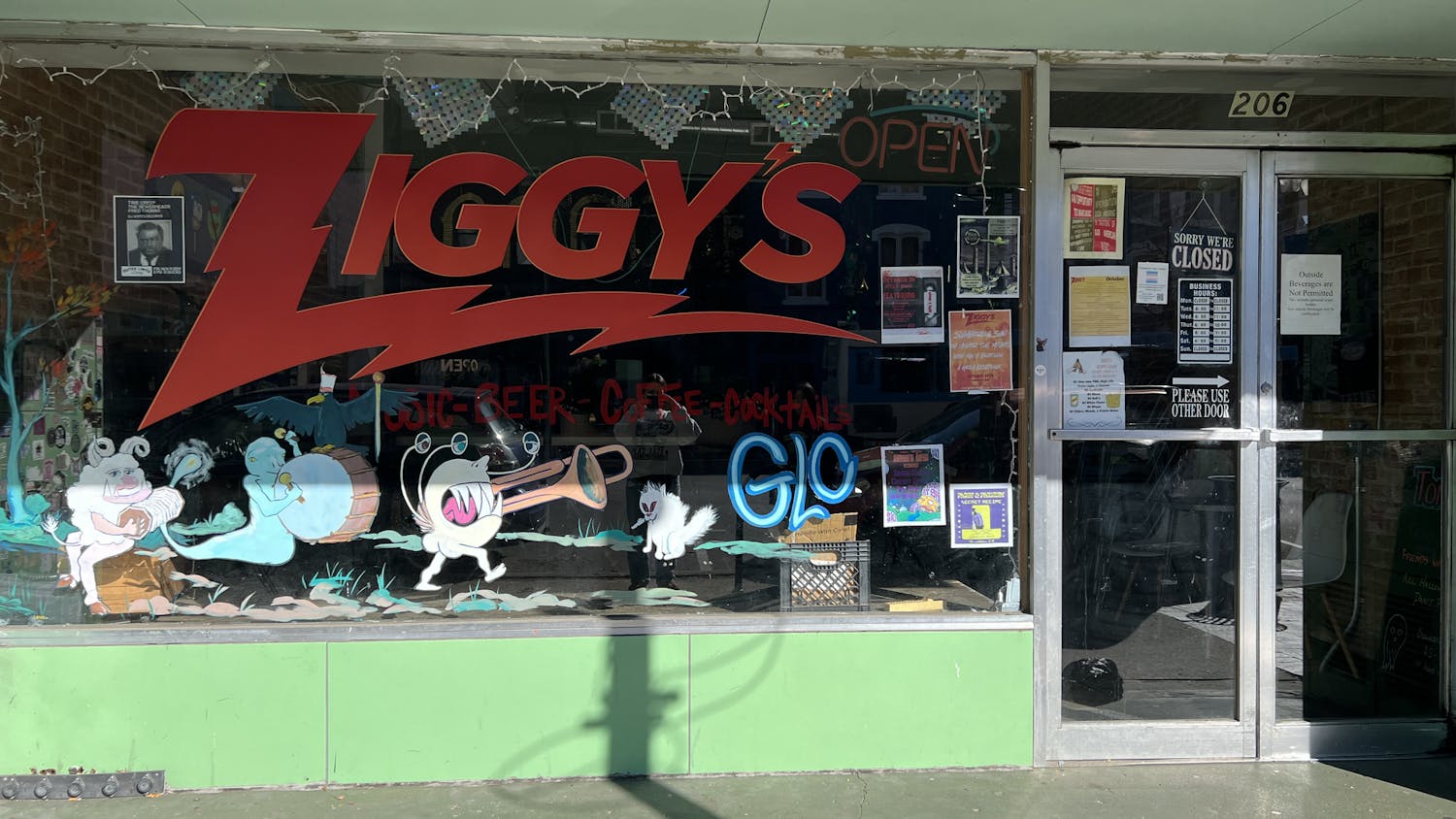 A storefront with the word "Ziggy's" written in big red letters on the building's glass wall. Underneath the writing are several colorful drawings of mythical creatures, some of them playing musical instruments. Off to the right are two glass double doors that are the entrance to the building.