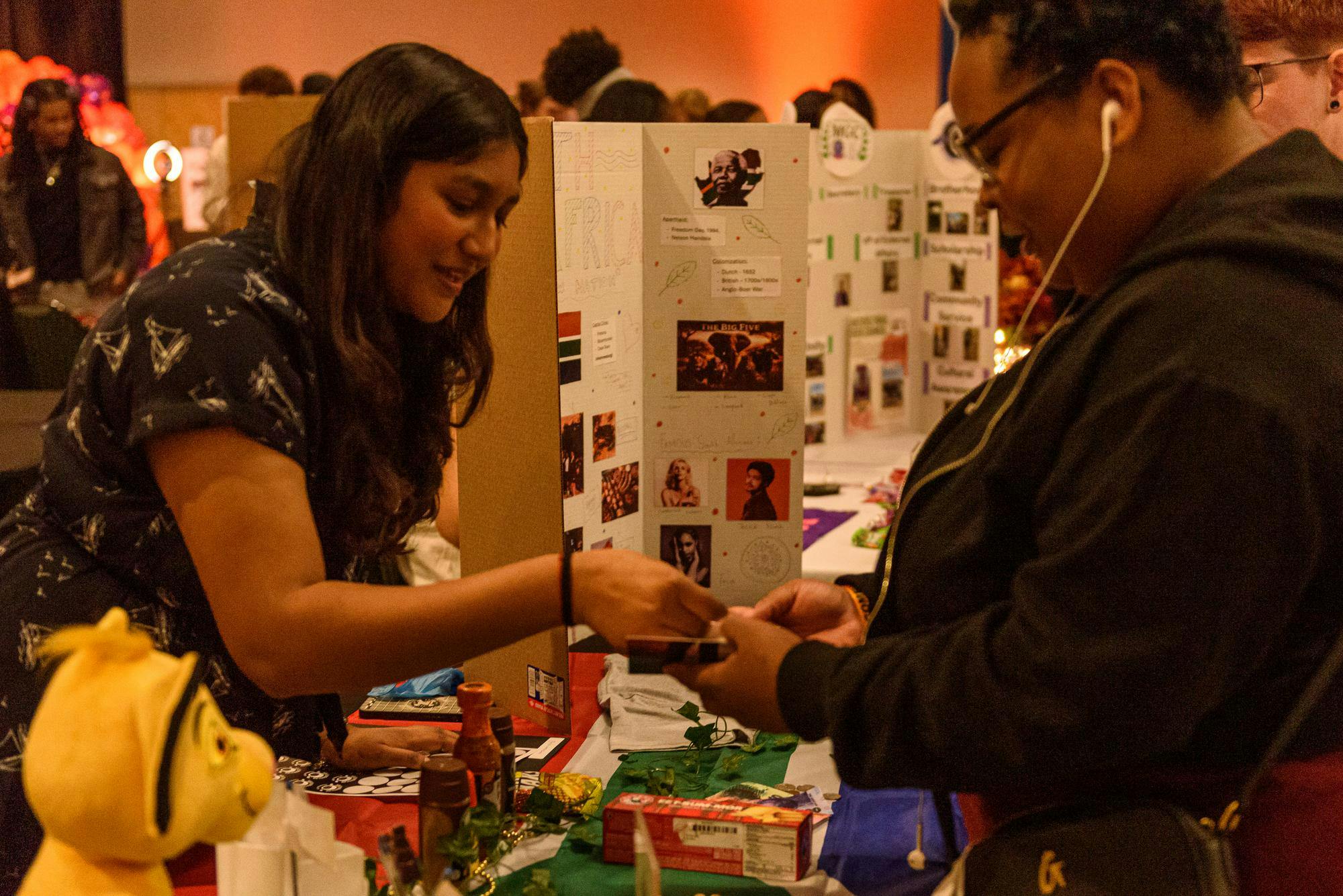 A person behind an event booth places a sticker into another persons booklet.