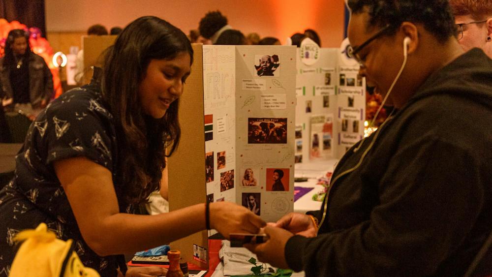 A person behind an event booth places a sticker into another persons booklet.