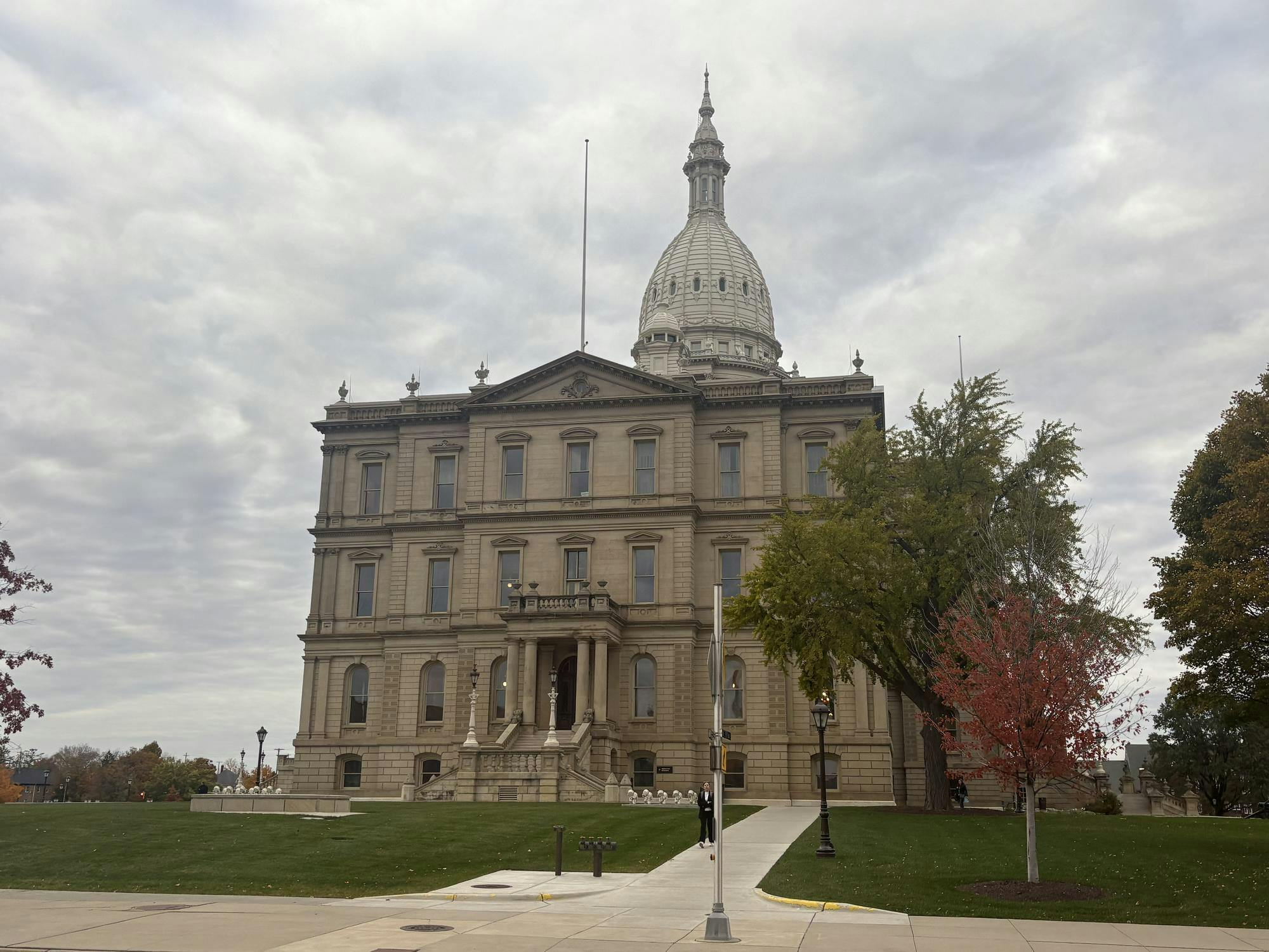 The State Capitol building sits on a grassy lawn next to trees.
