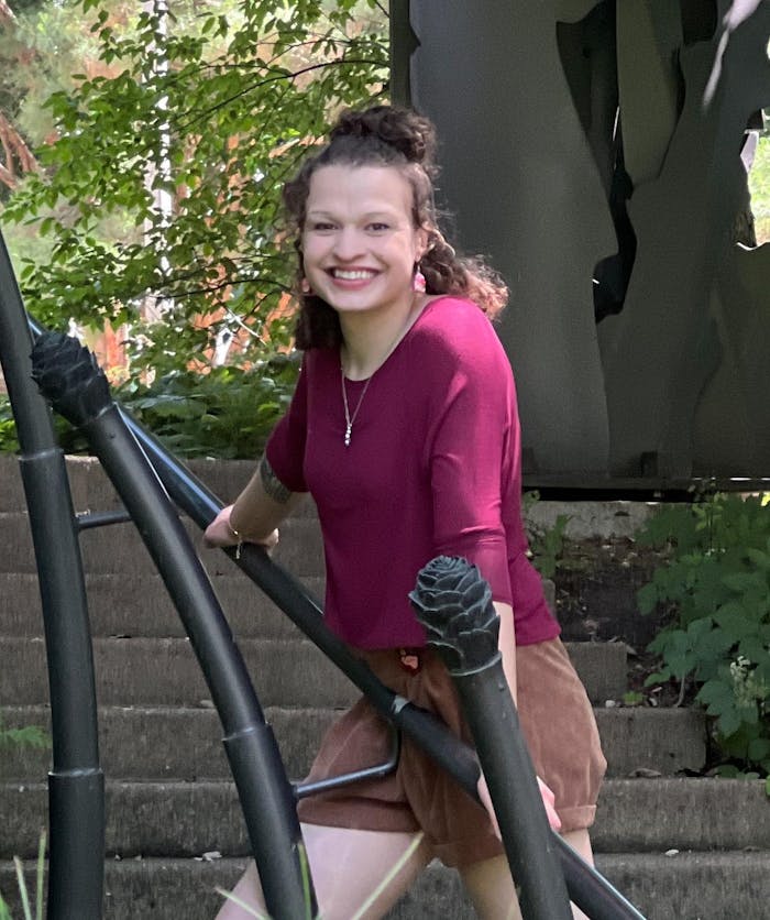 Headshot of Laura Meriweather, standing on an outdoor staircase and leaning on the railing, from the waist-up.
