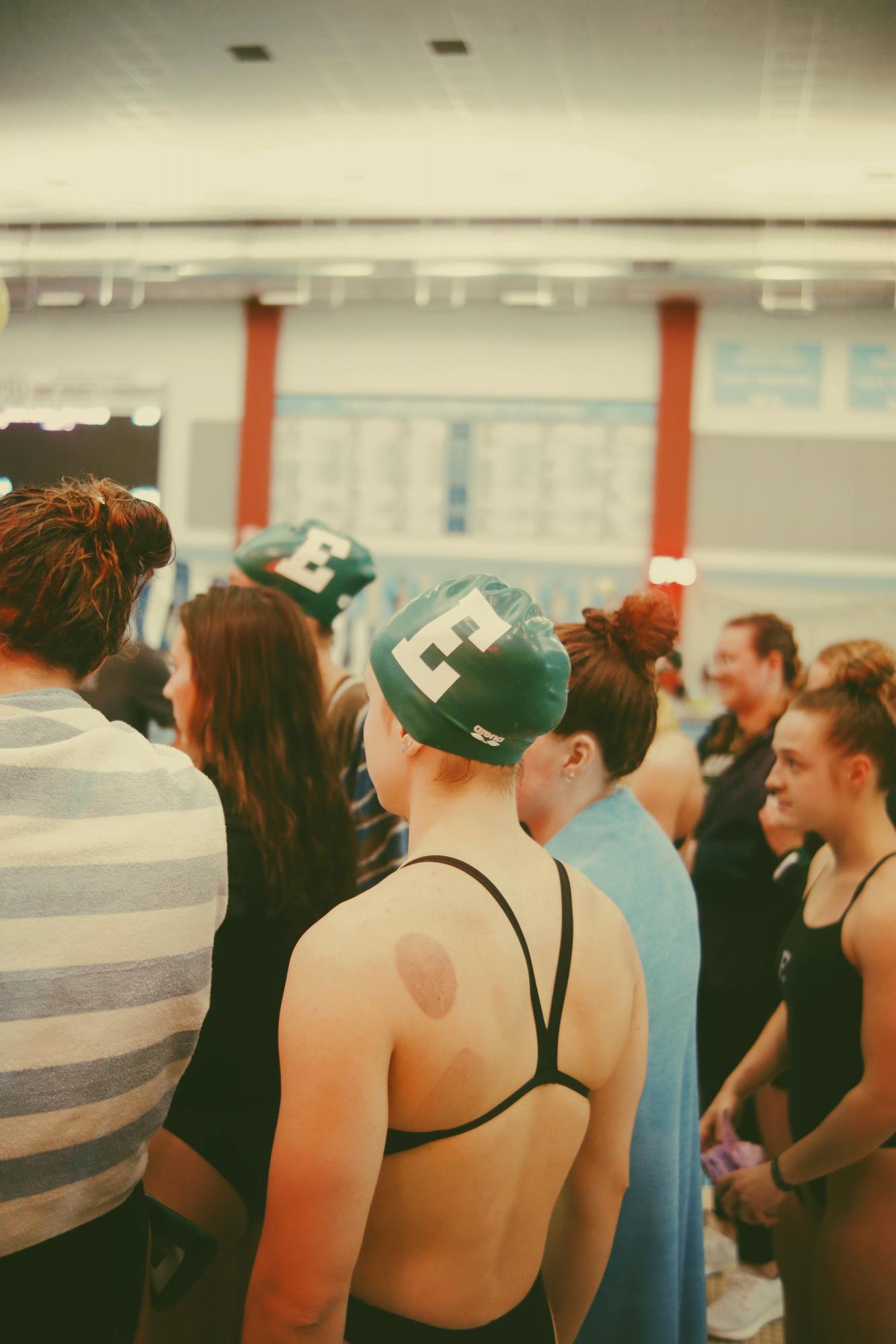 Several swimmers are pictured together from the shoulders up. They face the same direction as if they are listening to someone speak off camera.