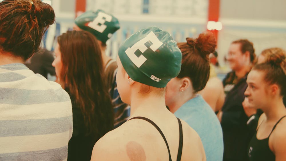 Several swimmers are pictured together from the shoulders up. They face the same direction as if they are listening to someone speak off camera.