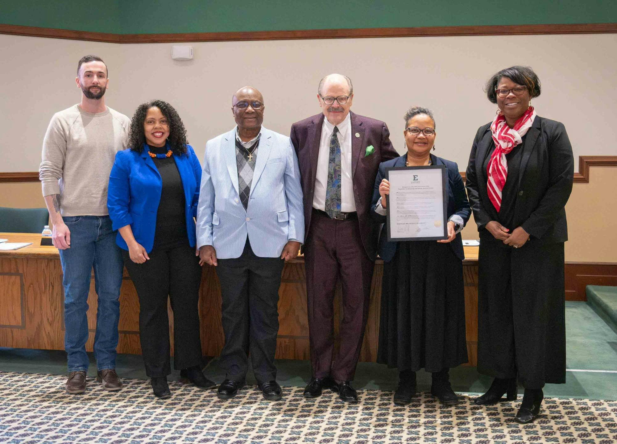 A line of six people smiling with one holding an award plaque.