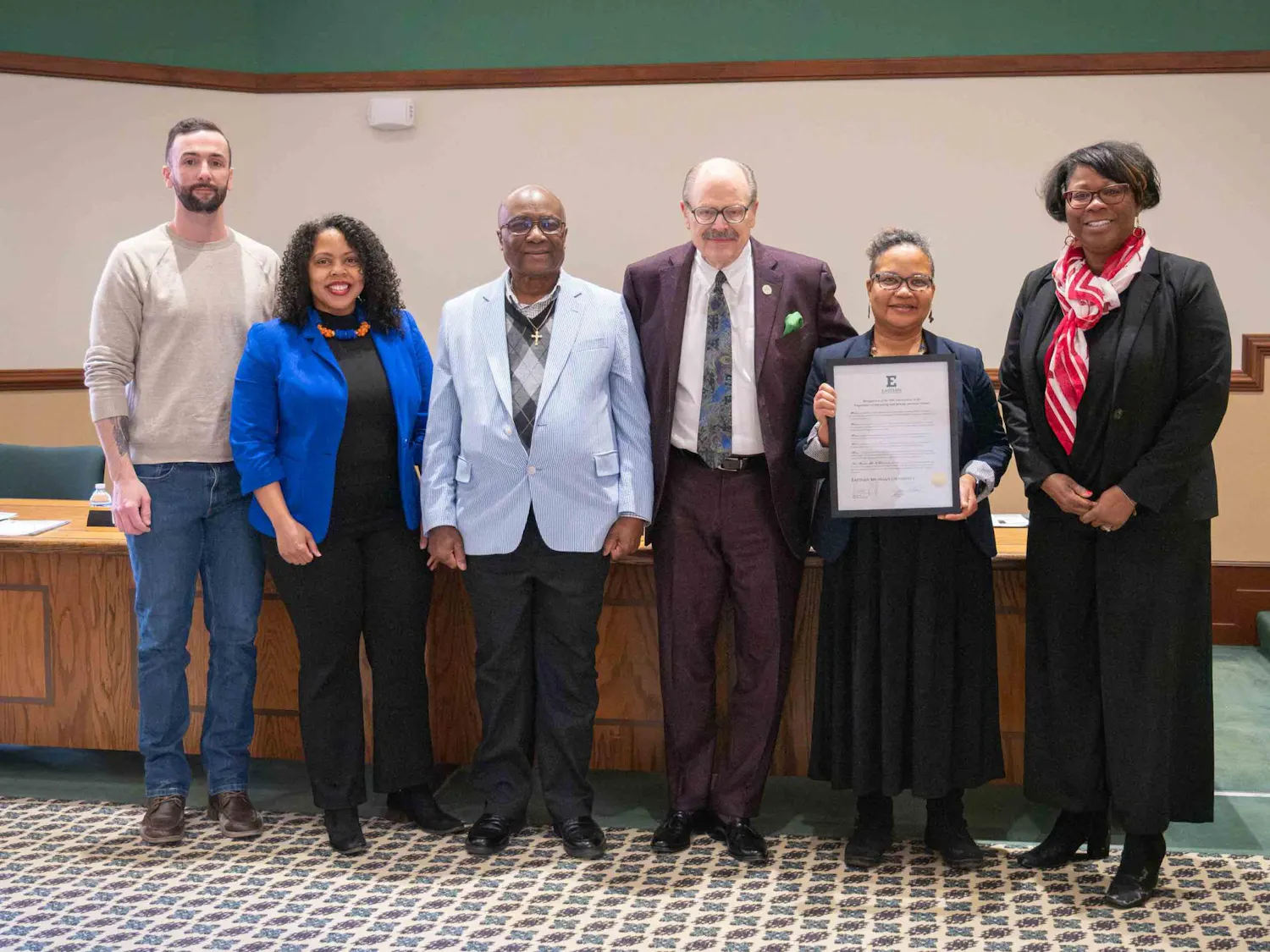 A line of six people smiling with one holding an award plaque.