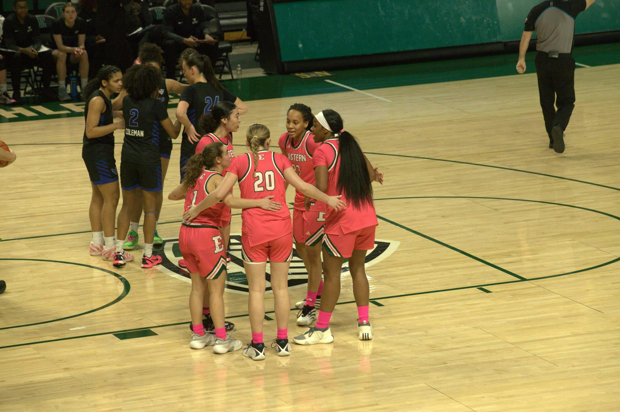 Women's basketball players huddle on an indoor court.