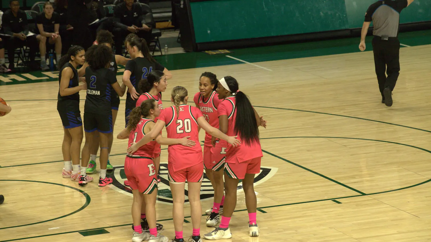 Women's basketball players huddle on an indoor court.