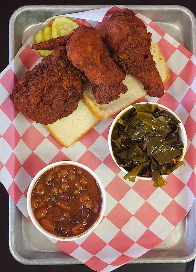 A fried chicken plate. On top are three pieces of fried chicken with a spicy glaze. On the middle right is the collard greens dish, and on the bottom left side, there is the cooked beans dish.