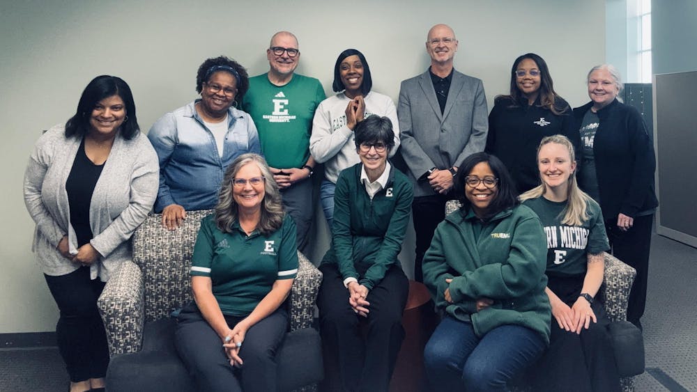 A group of people, many wearing EMU logo clothing, smile for a photo in an office space.