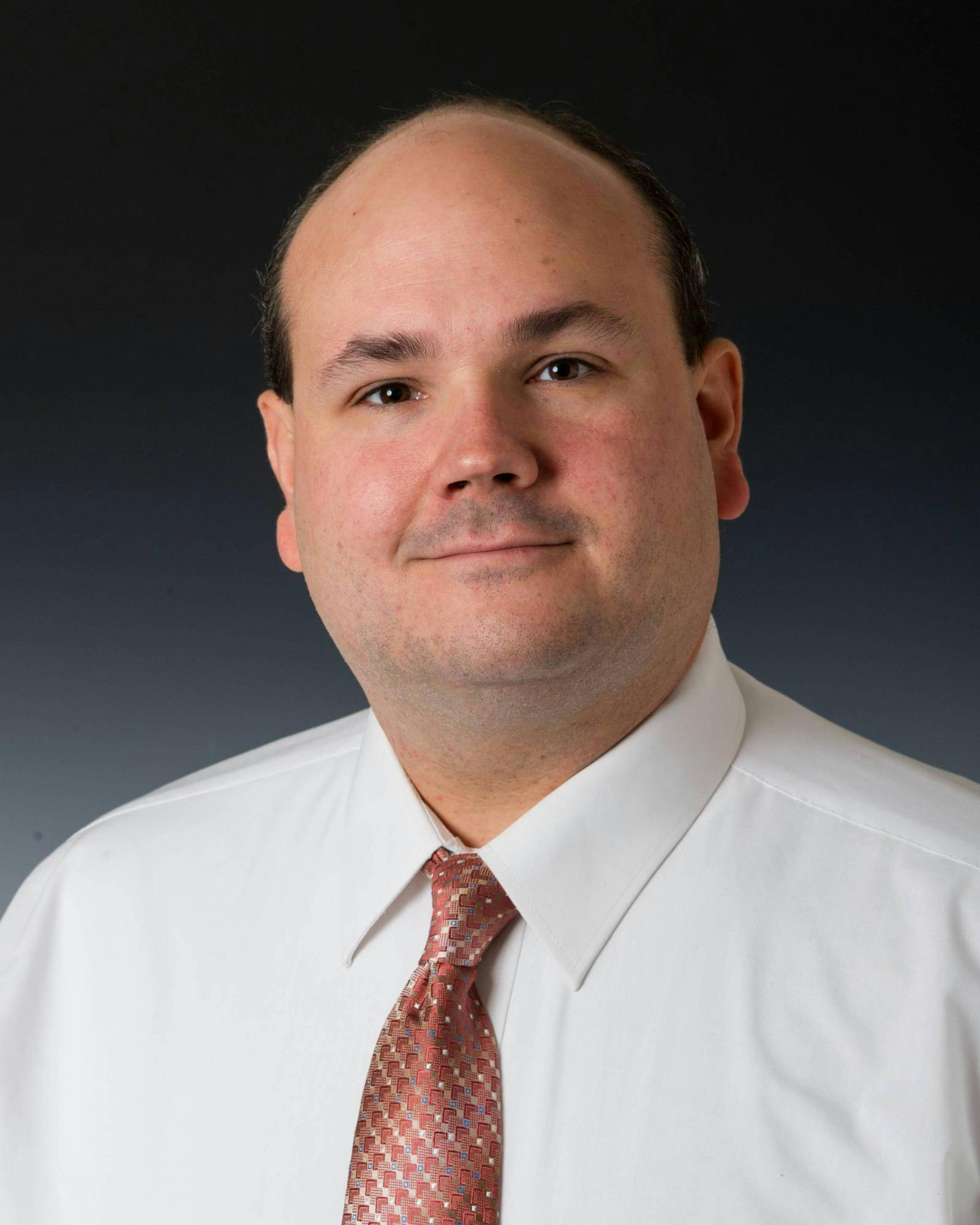 Headshot of Tom Kasper smiling in front of a black background. 