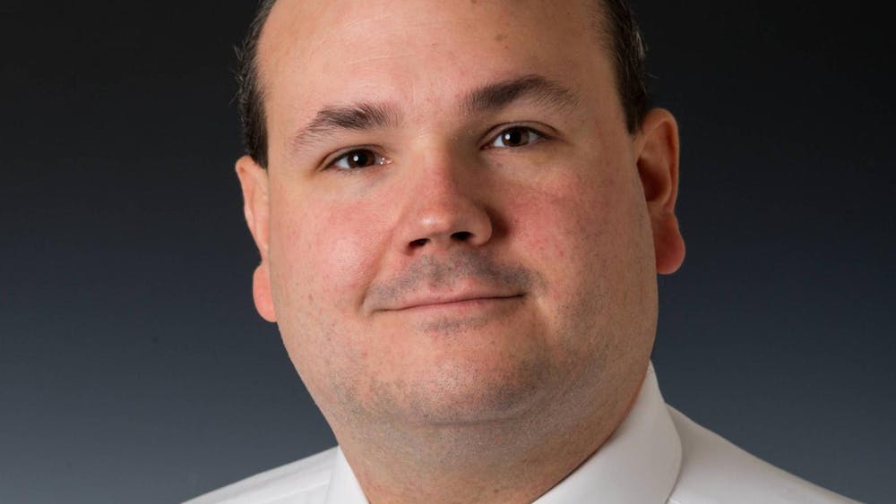 Headshot of Tom Kasper smiling in front of a black background.