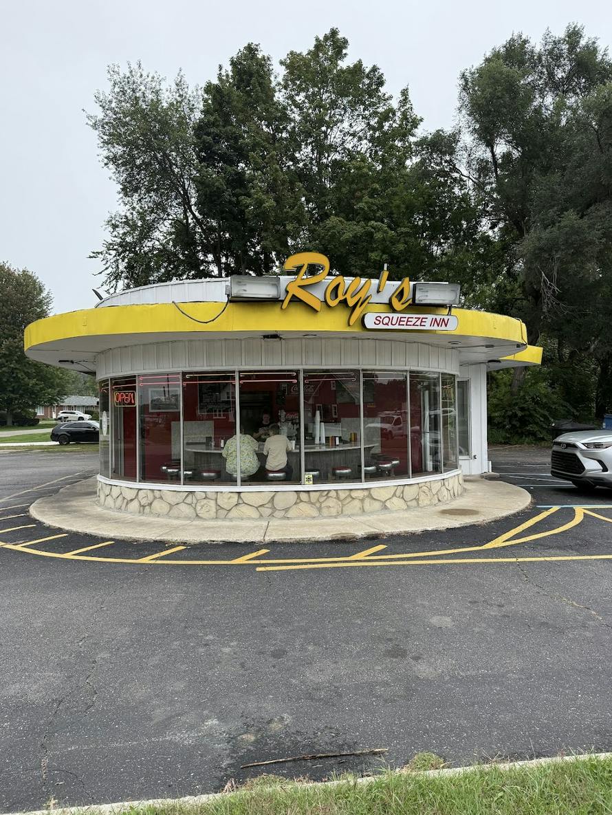 A circular building has large windows you can see people eating at a counter at.
