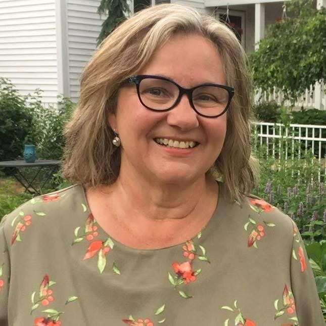 Carol Schlagheck smiles while outside with a garden and yard in the background.