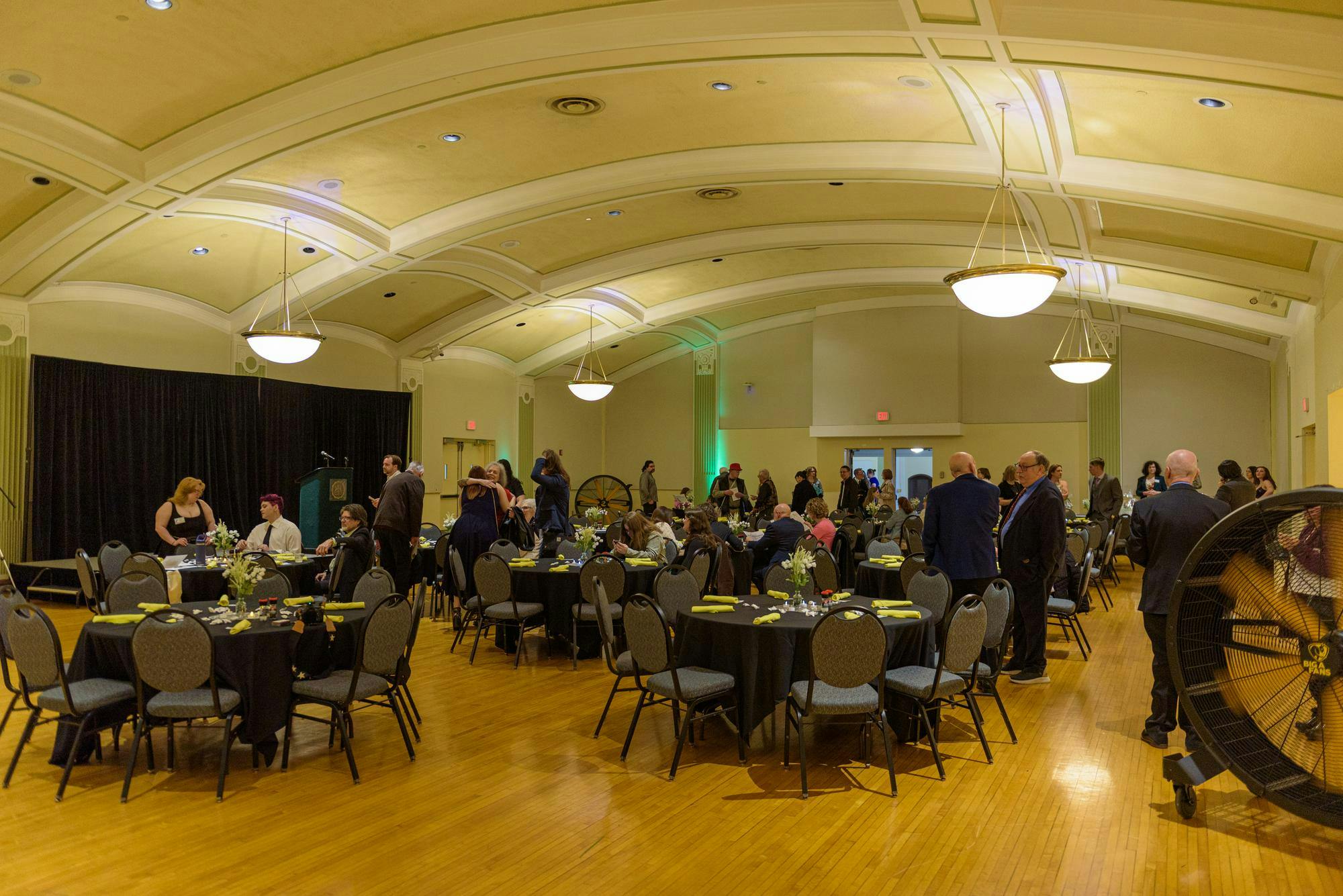 A room with black chairs and tables and people dressed in semi-formal attire.