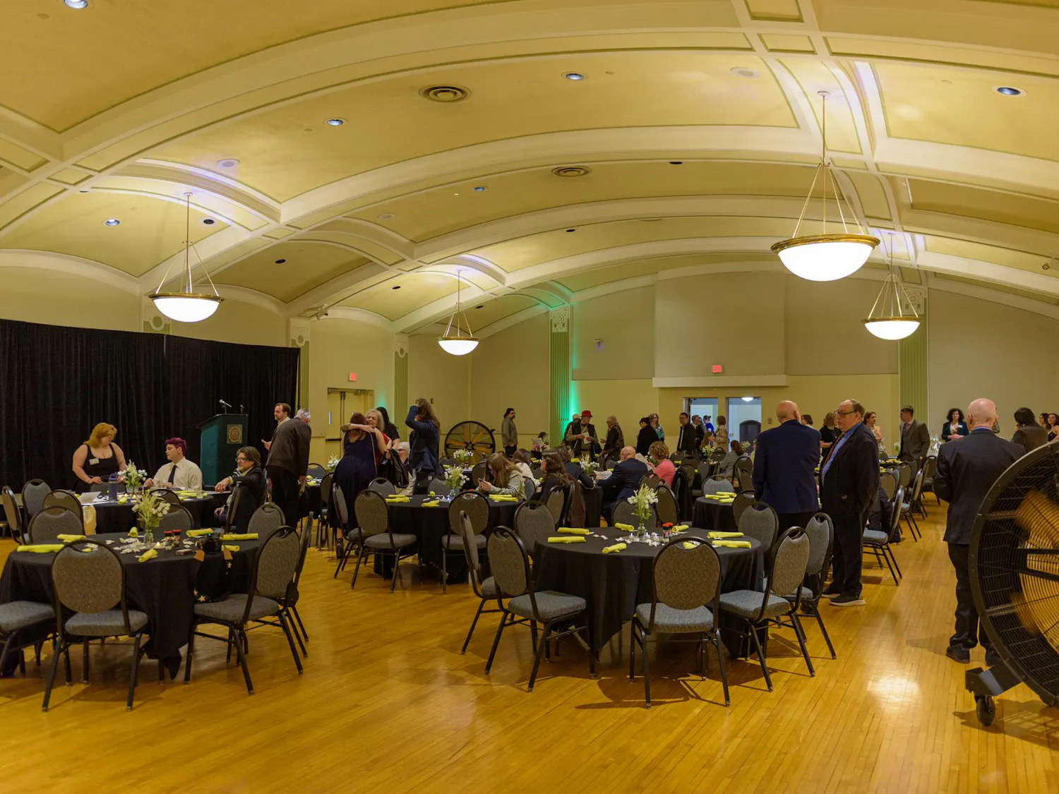 A room with black chairs and tables and people dressed in semi-formal attire.