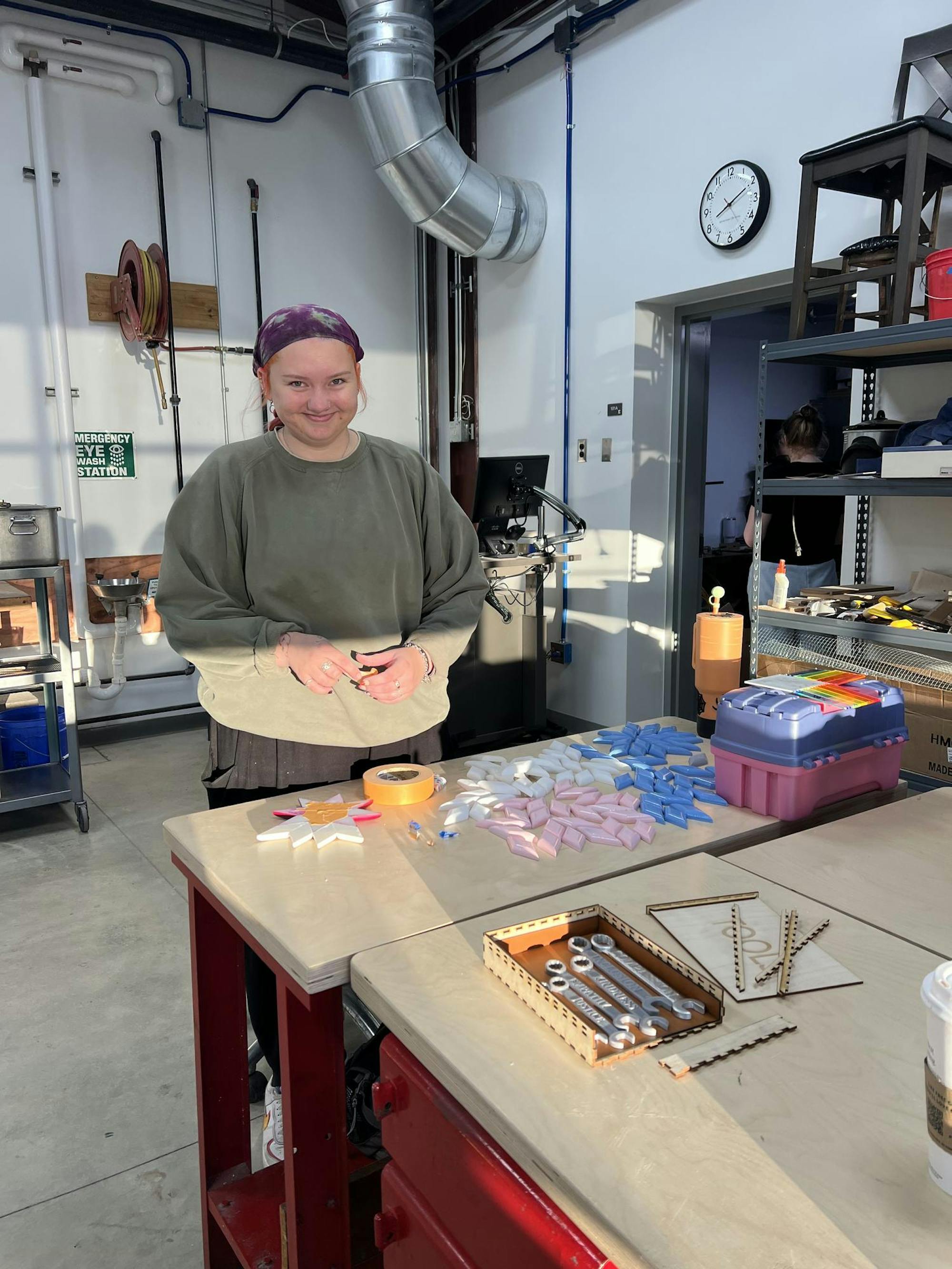 Chrissy Kuiper stands in an industrial art studio behind a metal table with small, colorful 3D-printed diamonds.