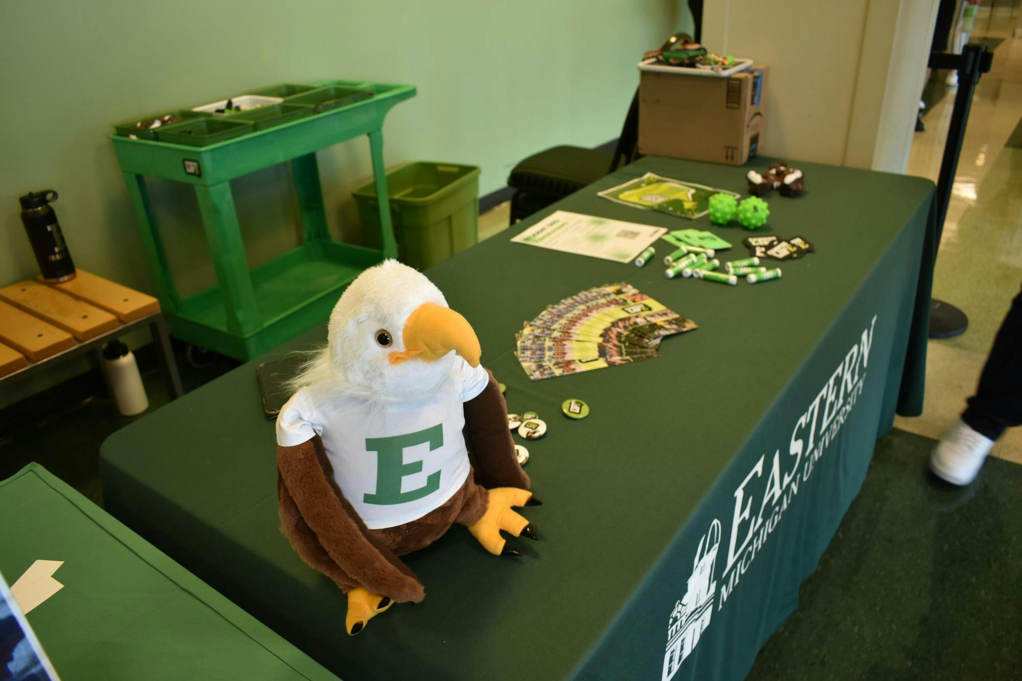 A welcome table with a green Eastern Michigan tablecloth and various EMU freebies. An eagle stuffed animal sits on the table close to the camera.