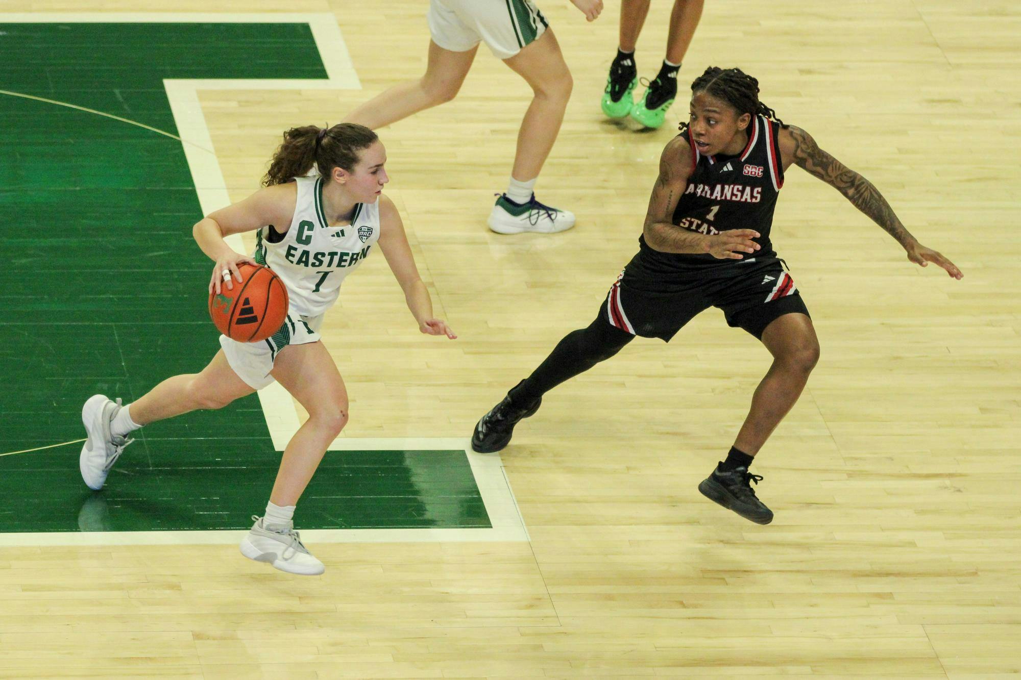 Eastern Michigan University women's basketball player, dribbling the basketball down the court with an opposing teammate nearly blocking her way.