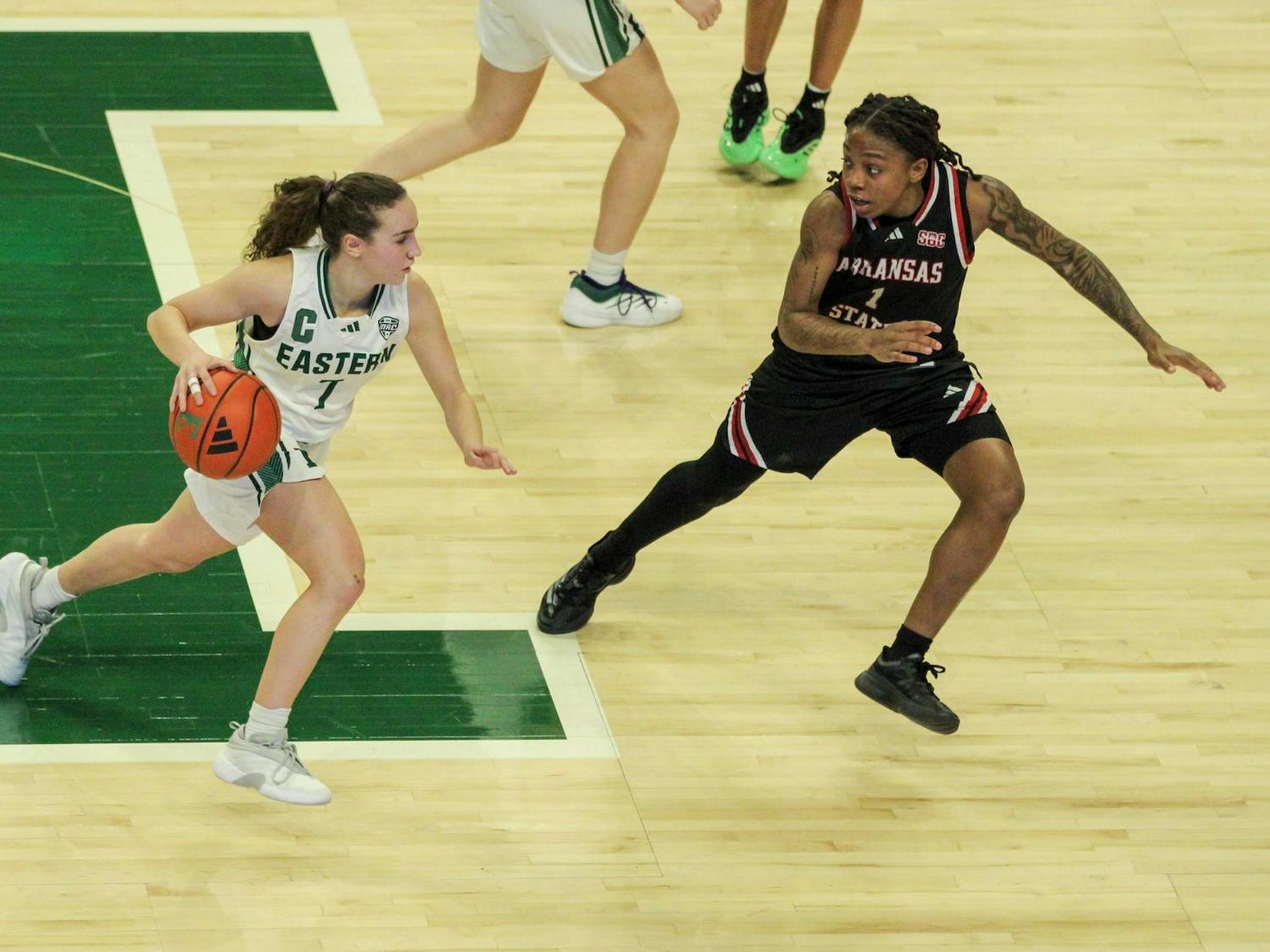 Eastern Michigan University women's basketball player, dribbling the basketball down the court with an opposing teammate nearly blocking her way.