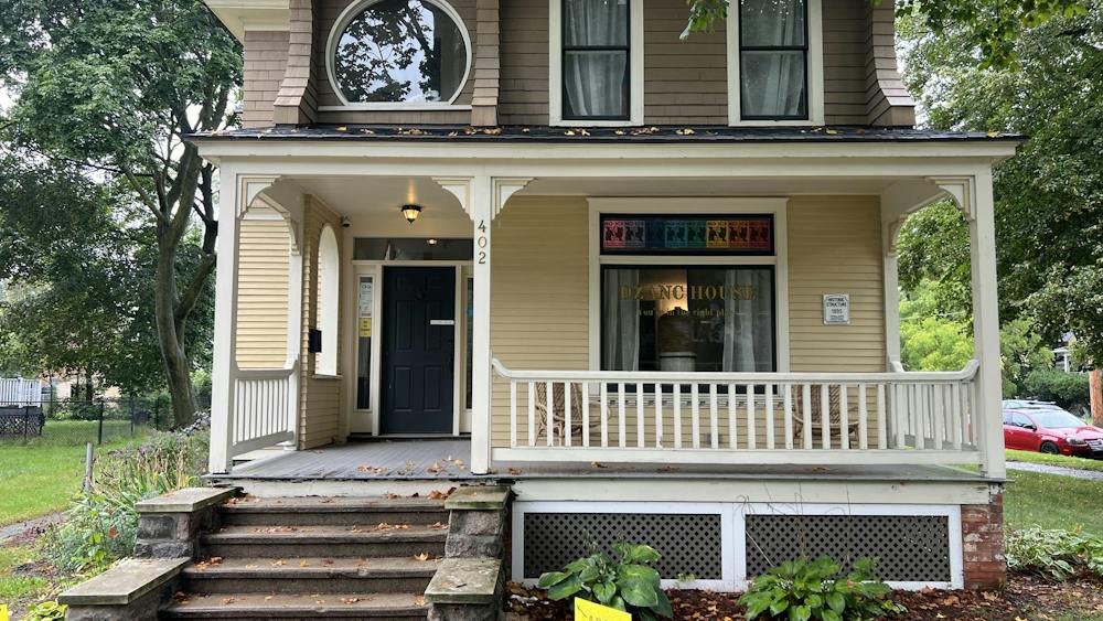 A two-story house is seen from the sidewalk, with the words "Dzanc House" on the front window.