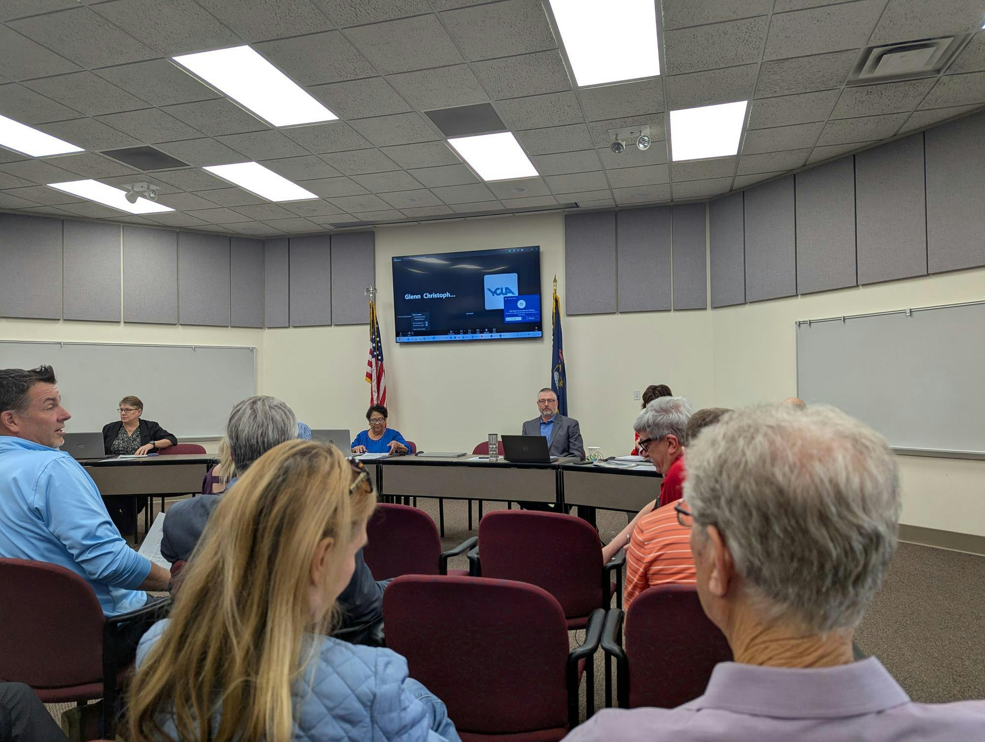 The backs of 6 audiene members face the camera. 5 Ypsilanti Township officials sit behind a shared desk in the background.
