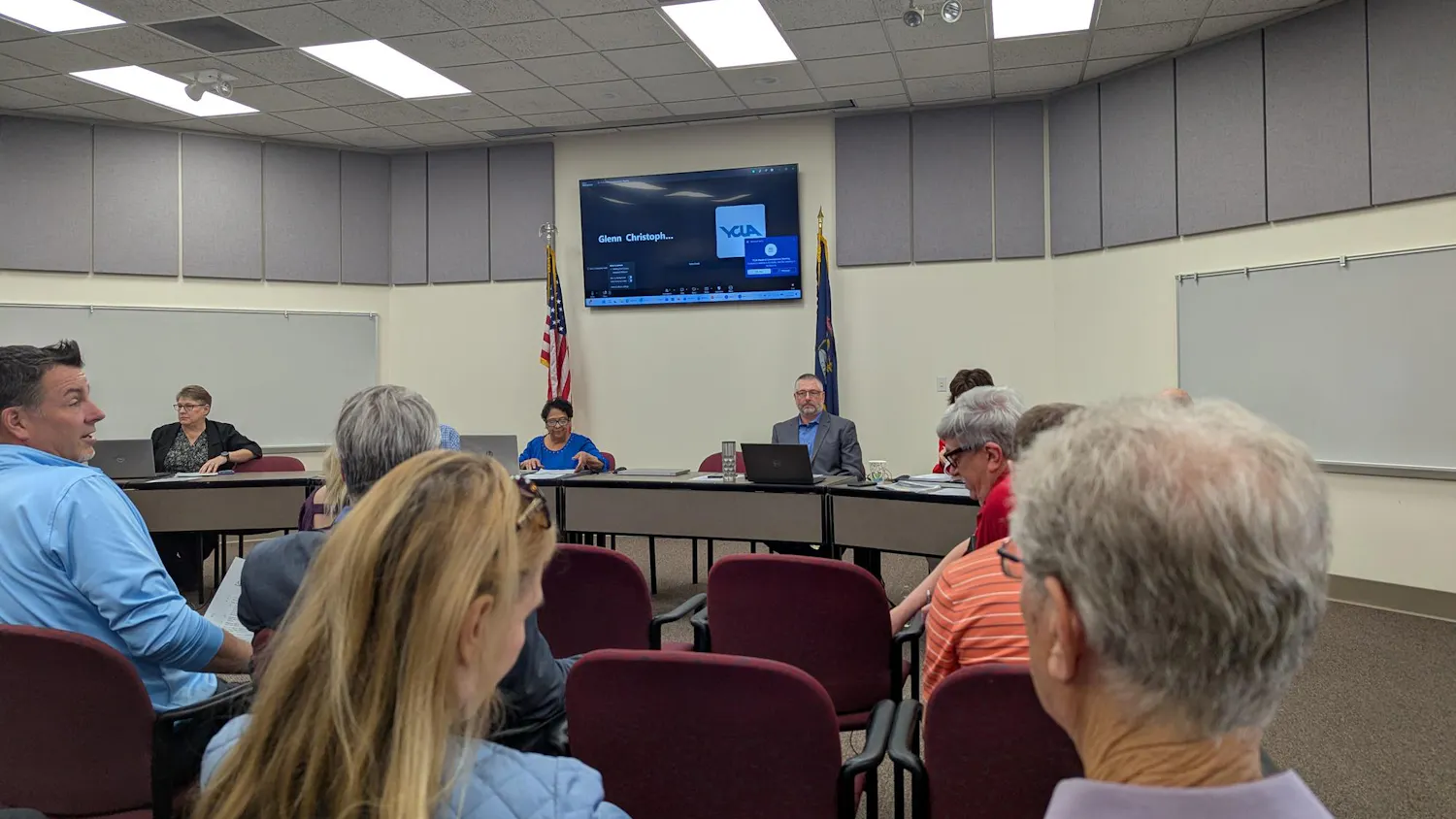 The backs of 6 audiene members face the camera. 5 Ypsilanti Township officials sit behind a shared desk in the background.