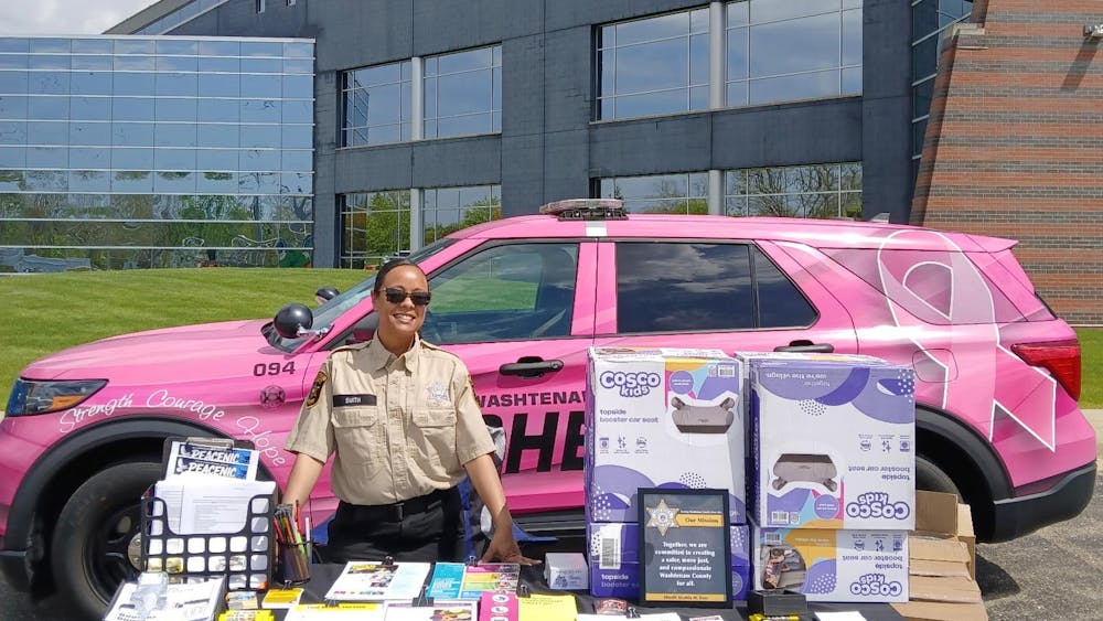 A woman stands at a table full of resources and car seats in front of a pink patrol car.