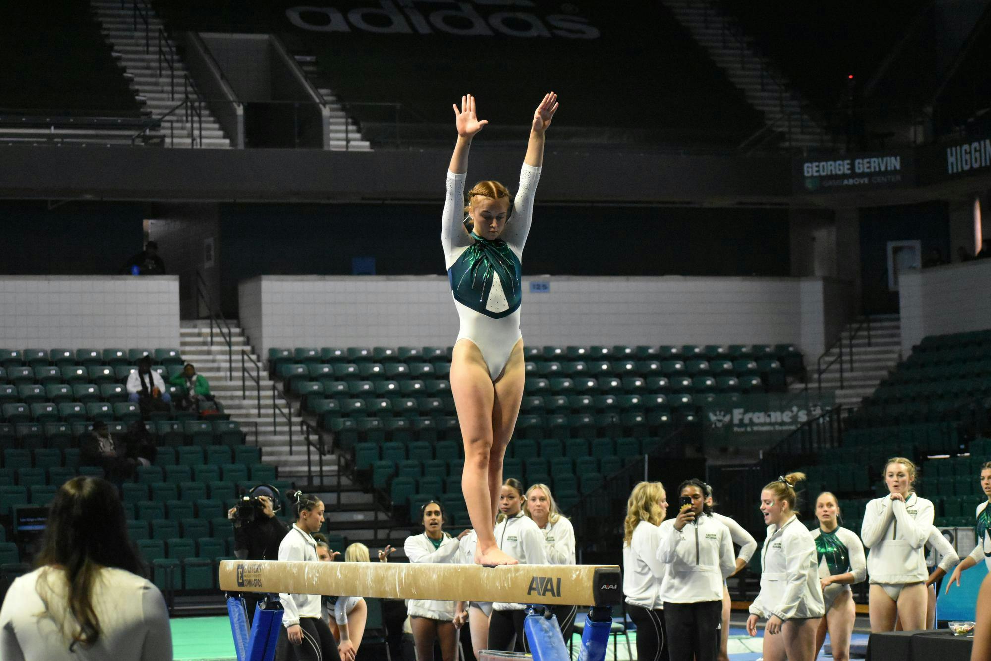 Gymnast Katin Childress stands on the beam. In the background her teammates cheer her on. 