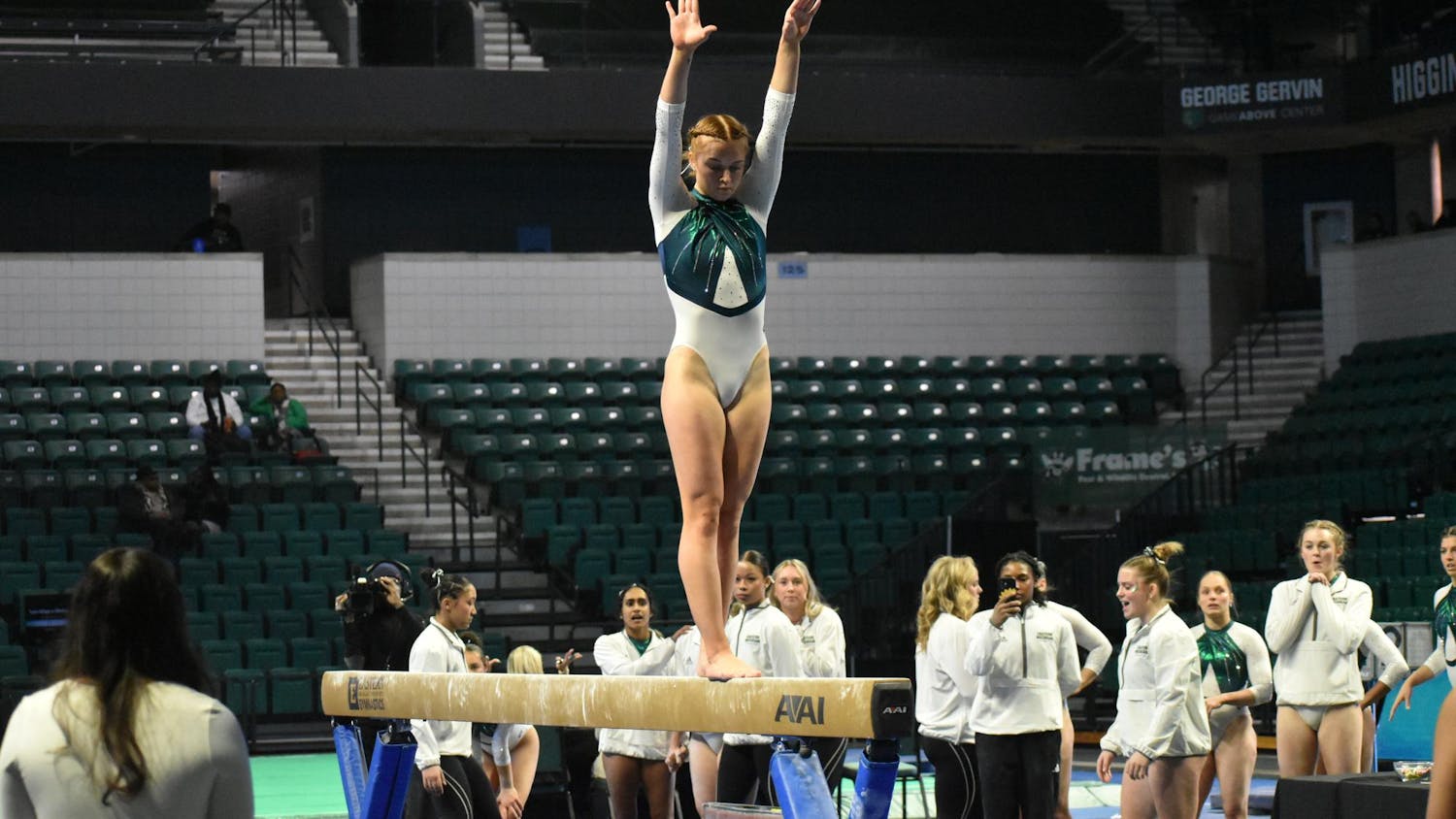 Gymnast Katin Childress stands on the beam. In the background her teammates cheer her on.