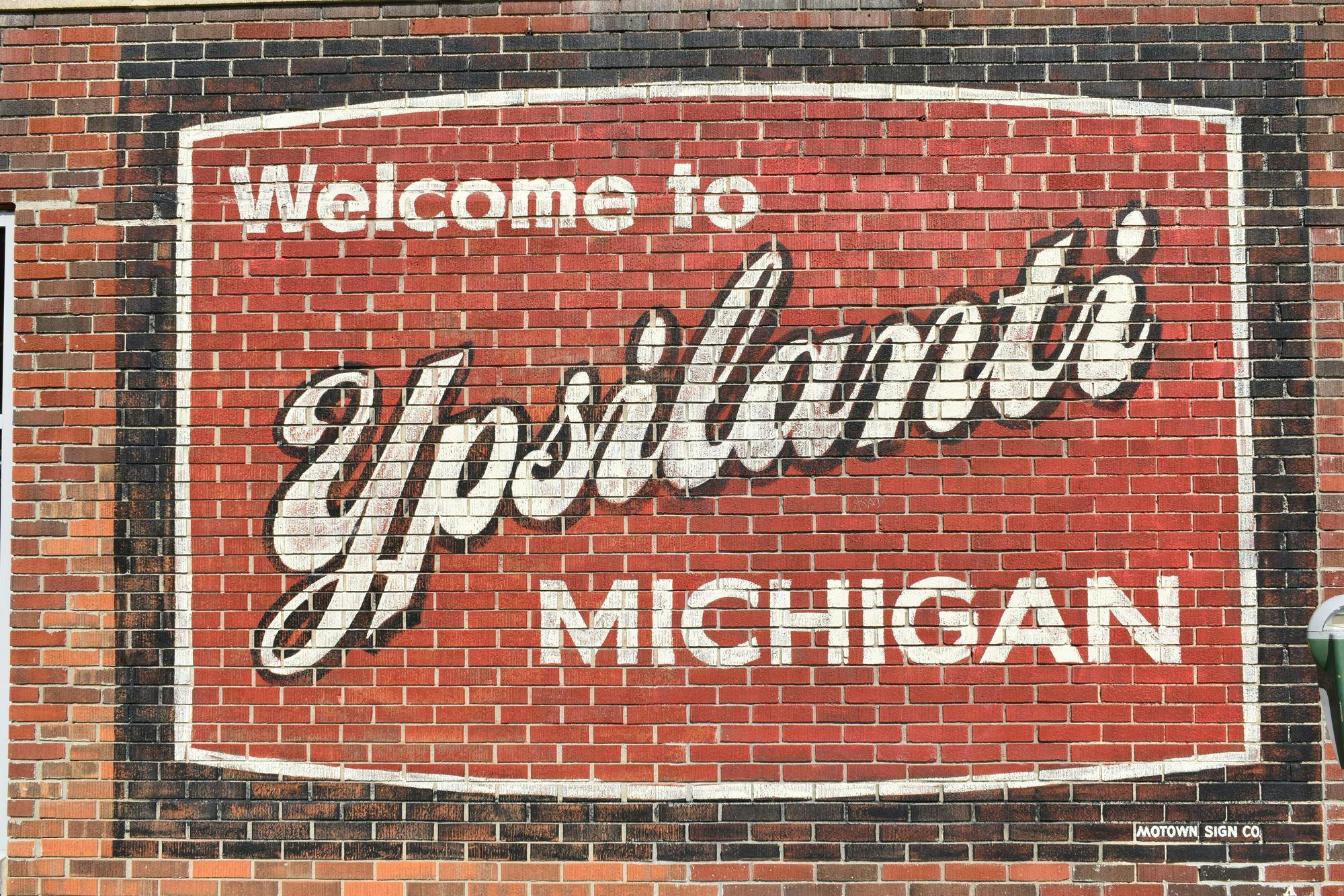 A red and black mural that says "Welcome to Ypsilanti Michigan" painted on a brick wall.