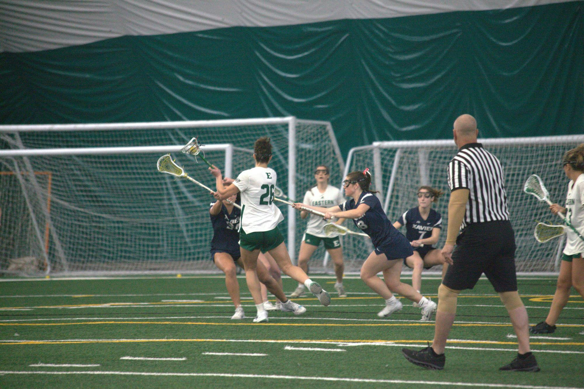 A women's lacrosse player dodges opposing team players, holding the ball out of their reach.