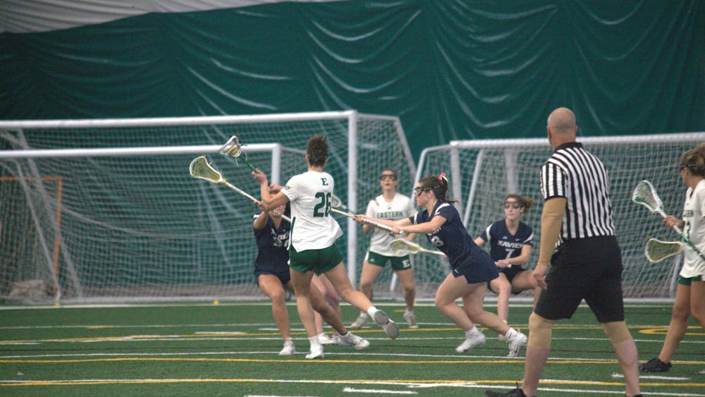 A women's lacrosse player dodges opposing team players, holding the ball out of their reach.