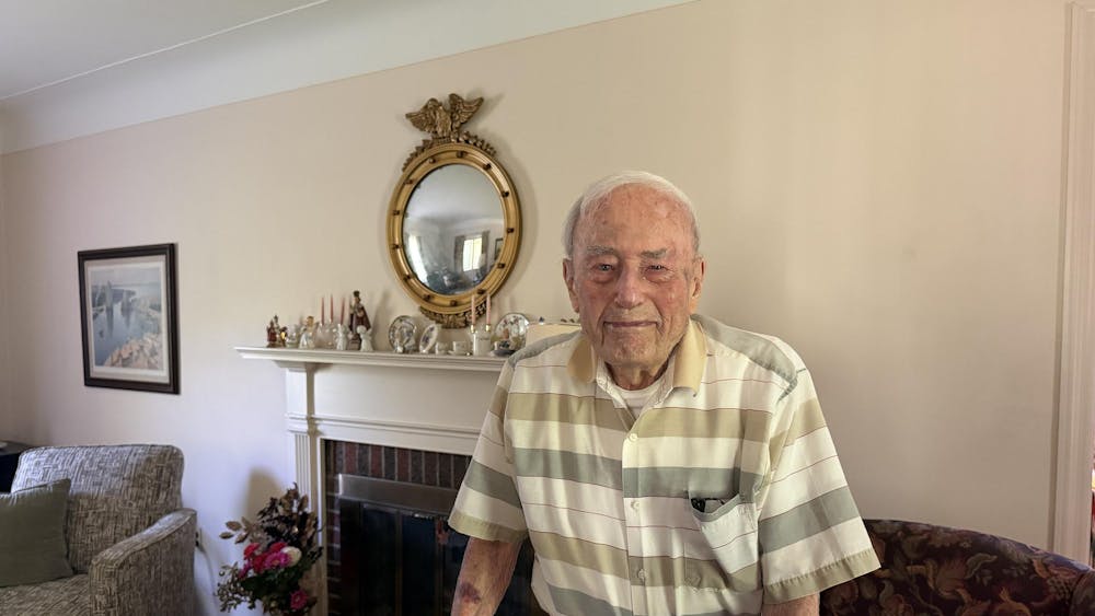 A man stands in his living room in front of a fireplace, holding on to his walker.