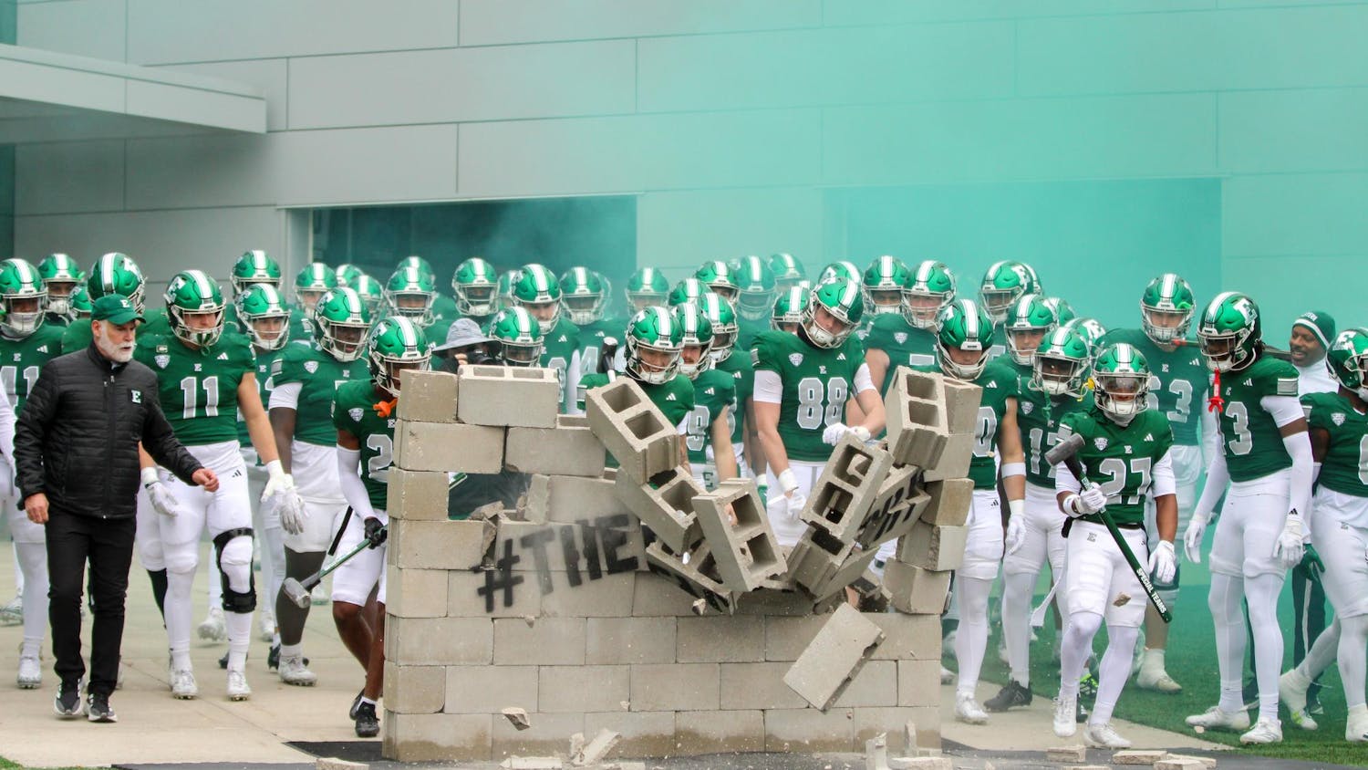 EMU Football team, in green jerseys, knock down the concrete wall