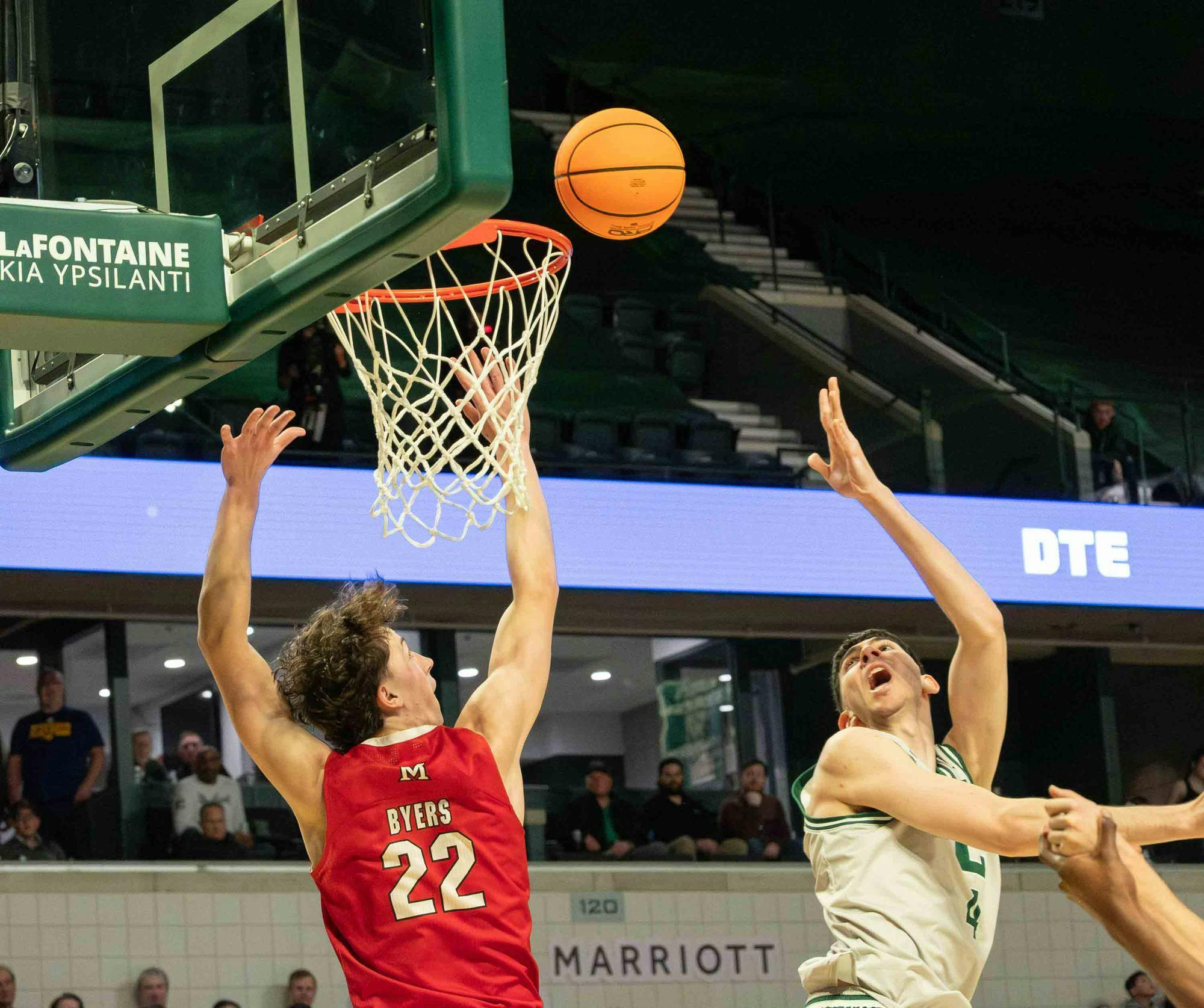 An EMU basketball players throws the basketball behind him towards the net.