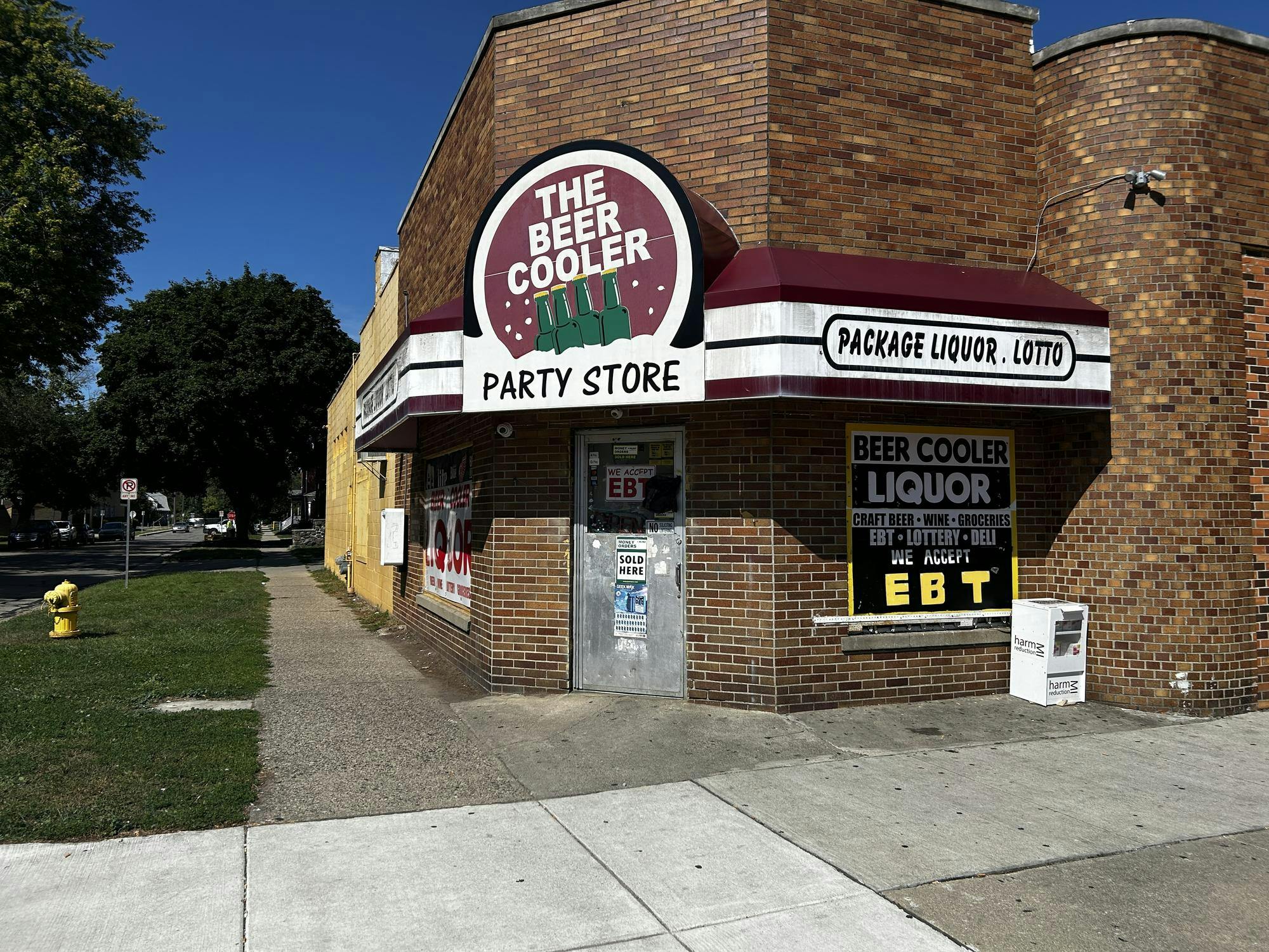 The storefront of The Beer Cooler, a downtown Ypsilanti business. It is a brick building with a gray door and a dark red and white awning. 