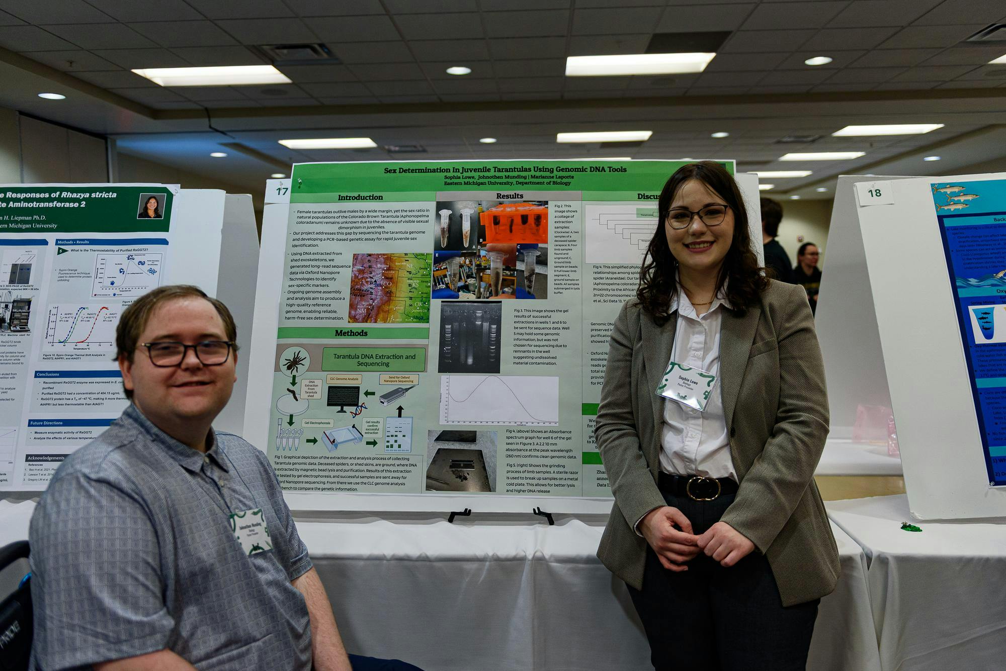 2 speakers standing next to a poster of a research project.