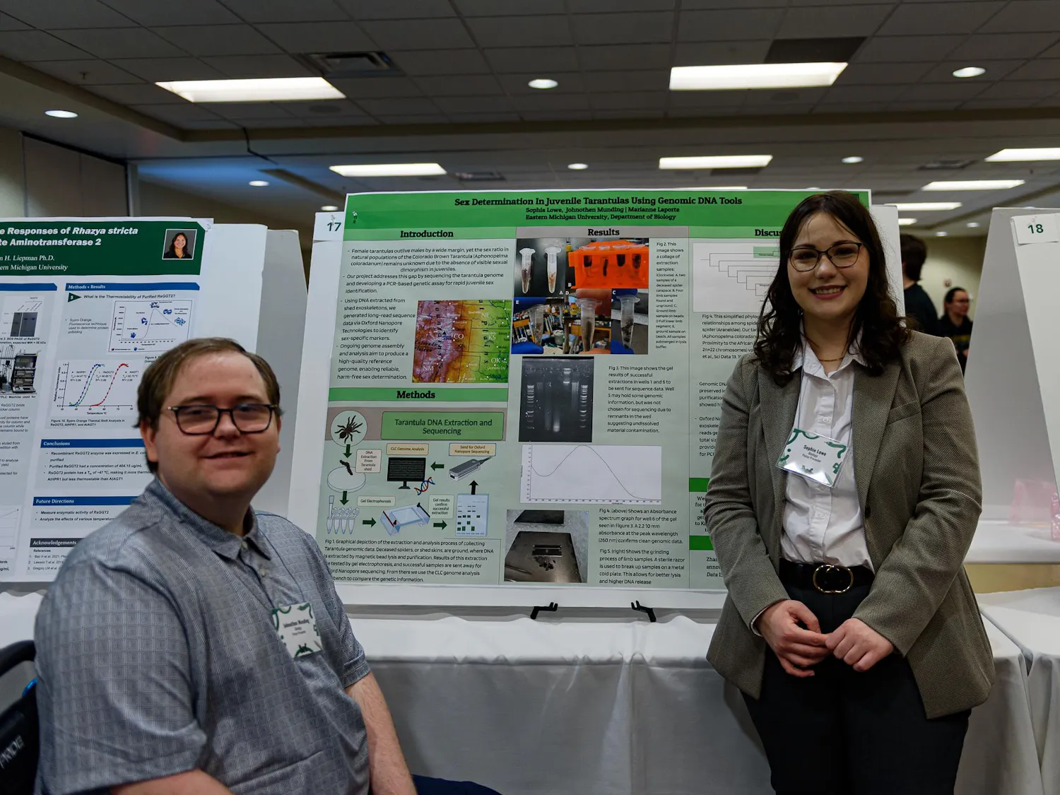 2 speakers standing next to a poster of a research project.