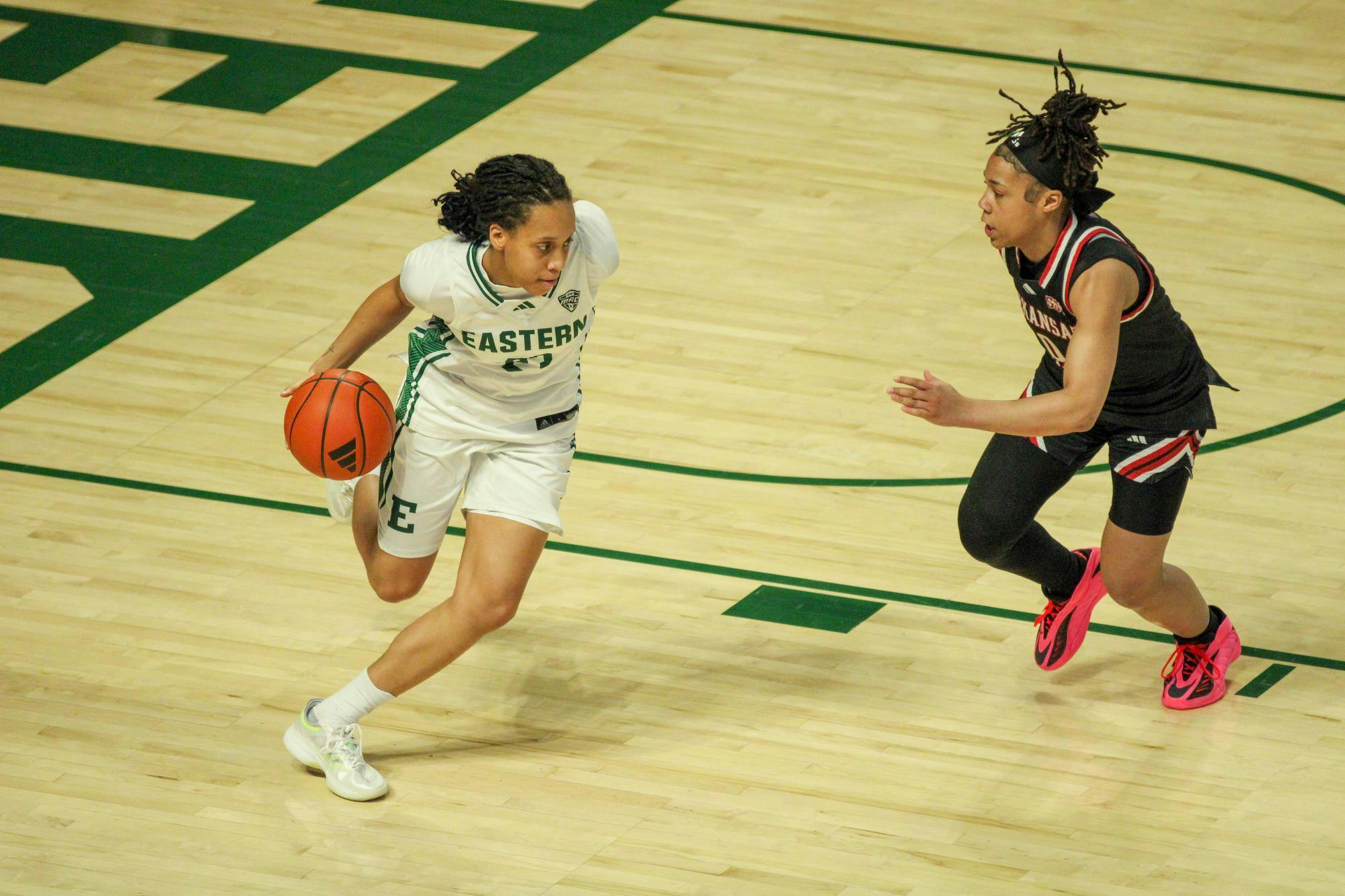 Eastern Michigan University women's player, in a white jersey, dribbling the ball with a Arkansas State player, in a black jersey, gaining on her.