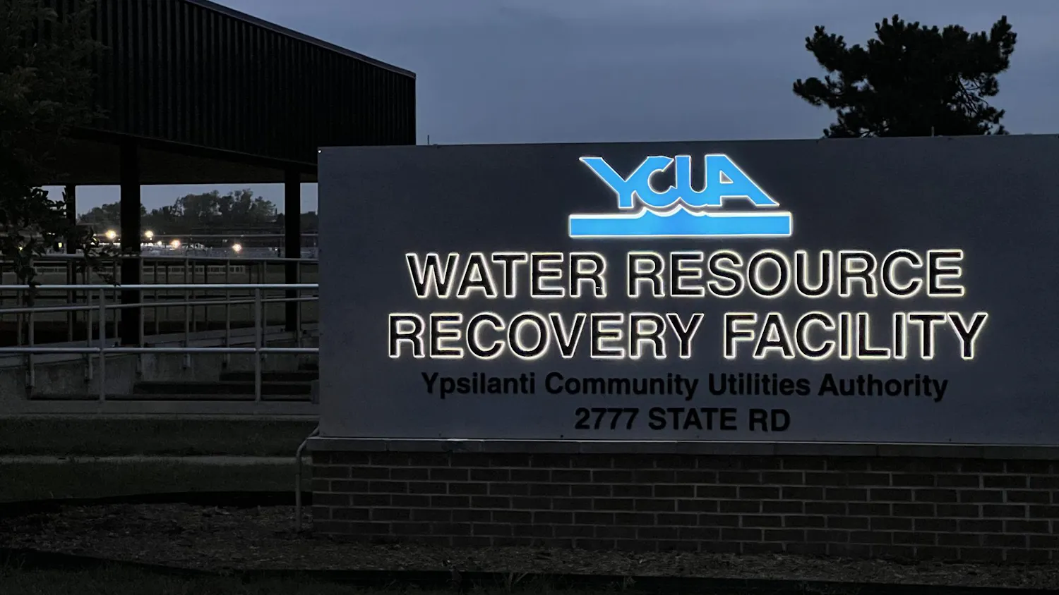 Lettering on the sign at 2777 State Rd glows at dusk, displaying the Ypsilanti Community Utilities Authority logo and the words "water resource recovery facility" underneath.