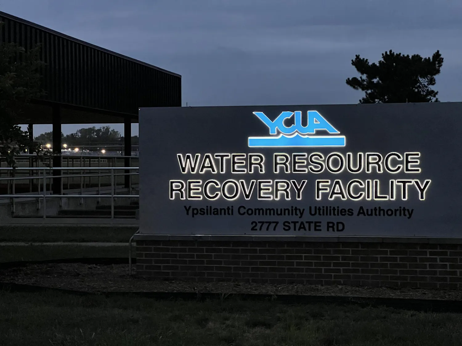 Lettering on the sign at 2777 State Rd glows at dusk, displaying the Ypsilanti Community Utilities Authority logo and the words "water resource recovery facility" underneath.