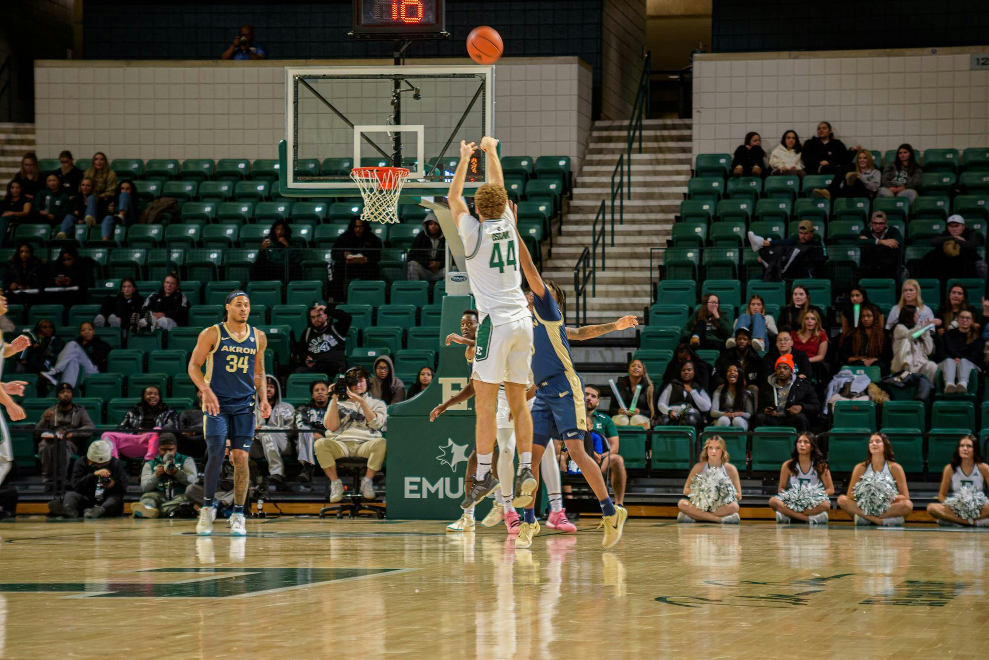 An Eastern Michigan men’s basketball player dressed in green and white shoots over an Akron defender wearing blue and gold.